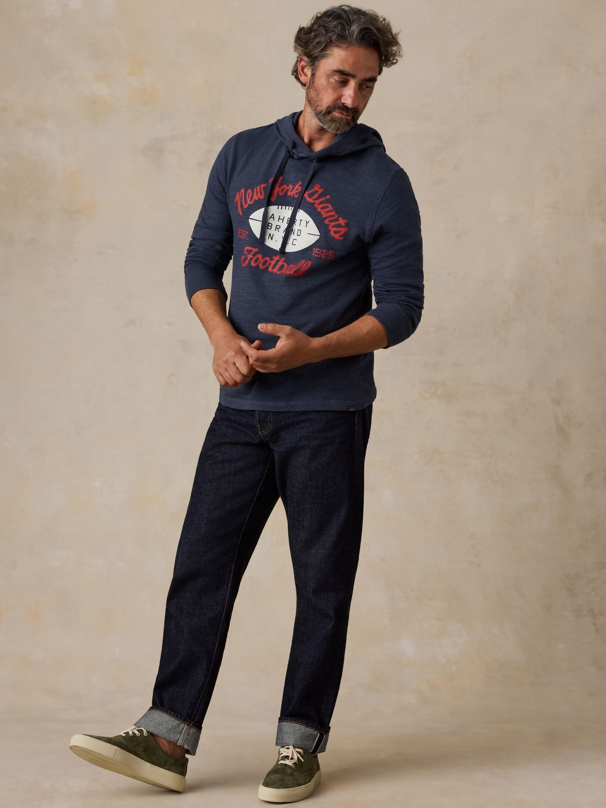 Man wearing a navy NY Giants hoodie, blue jeans, and green sneakers, image 2 of 6