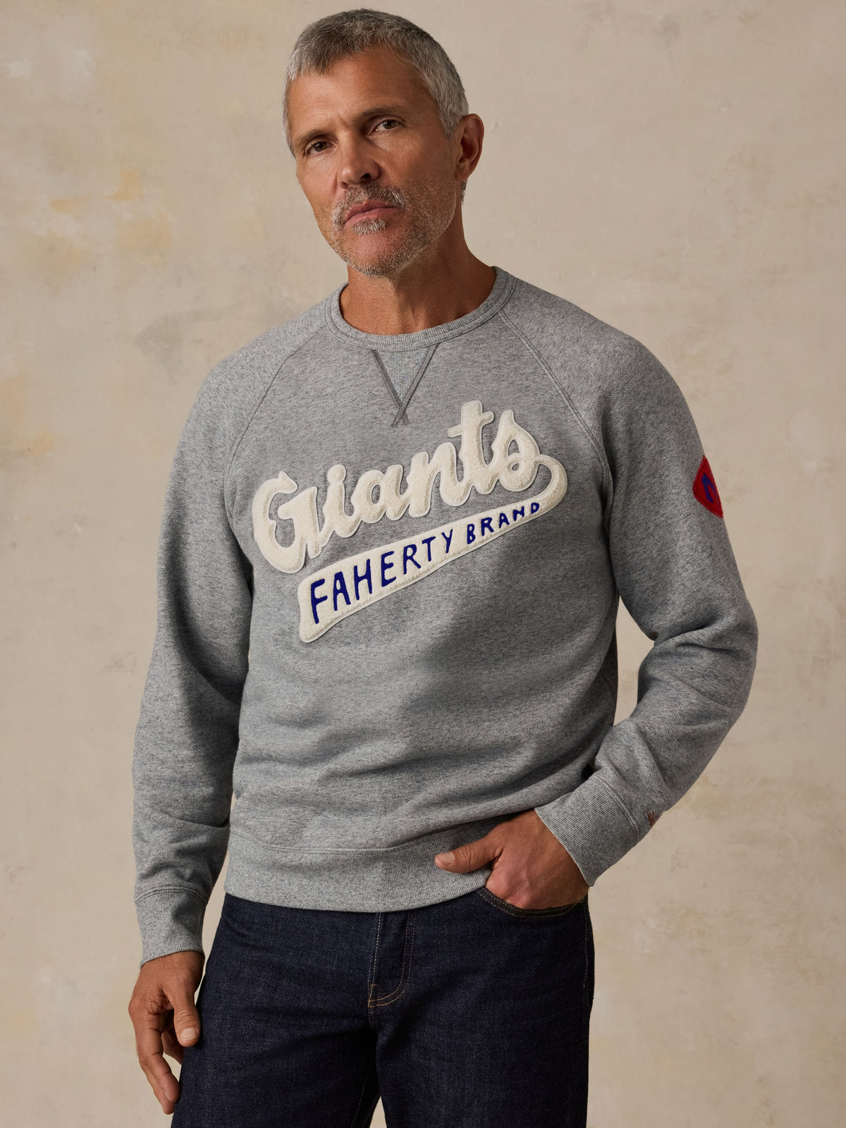 A man wearing a grey NY Giants crewneck and blue jeans, image 2 of 5