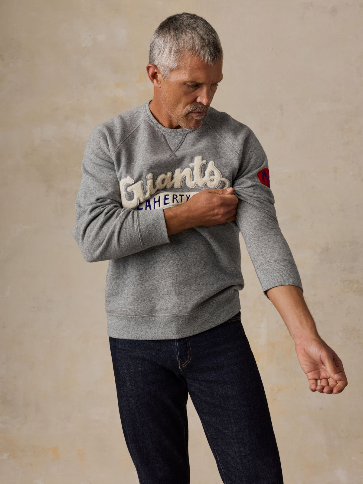A man wearing a grey NY Giants crewneck and blue jeans, image 5 of 5