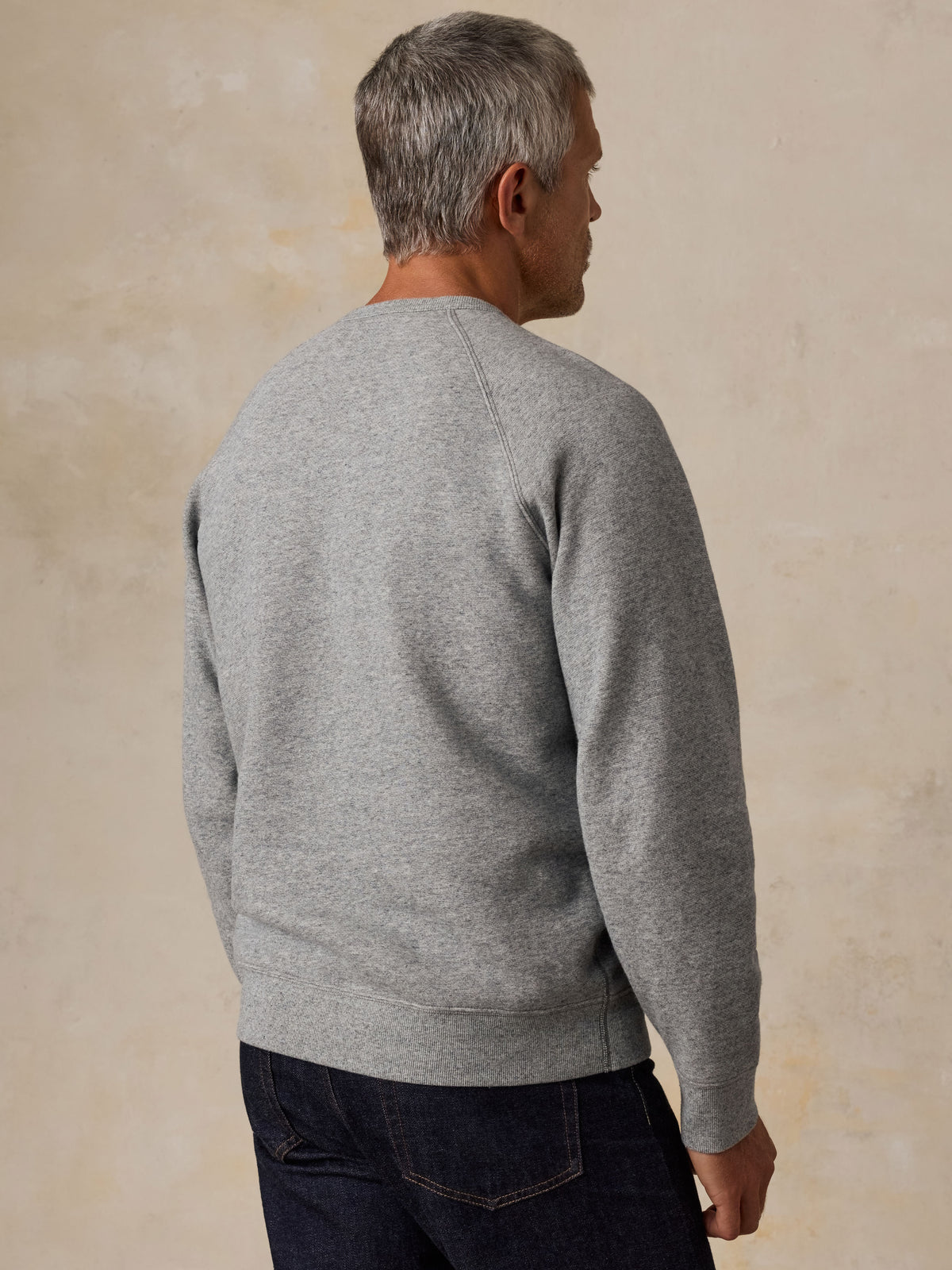 A man viewed from behind wearing a grey NY Giants crewneck and blue jeans, image 4 of 5