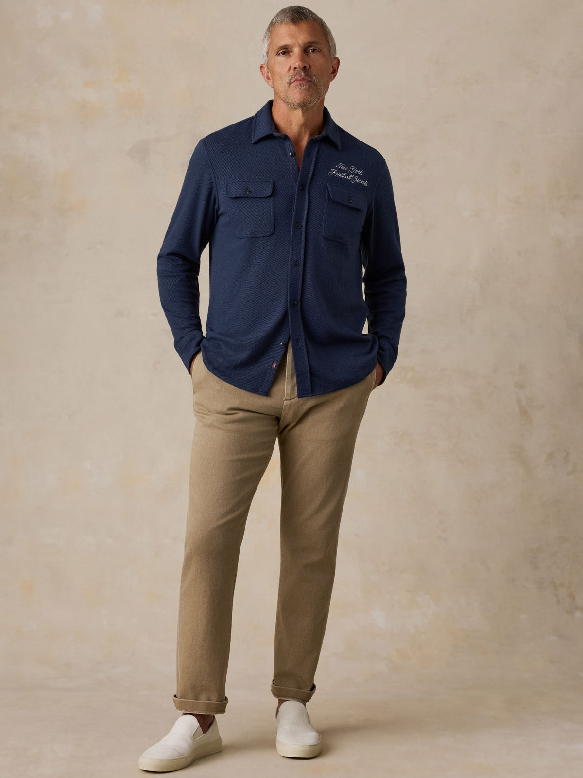 Man wearing a NY Giants button up shirt, beige pants, and white sneakers, image 1 of 7