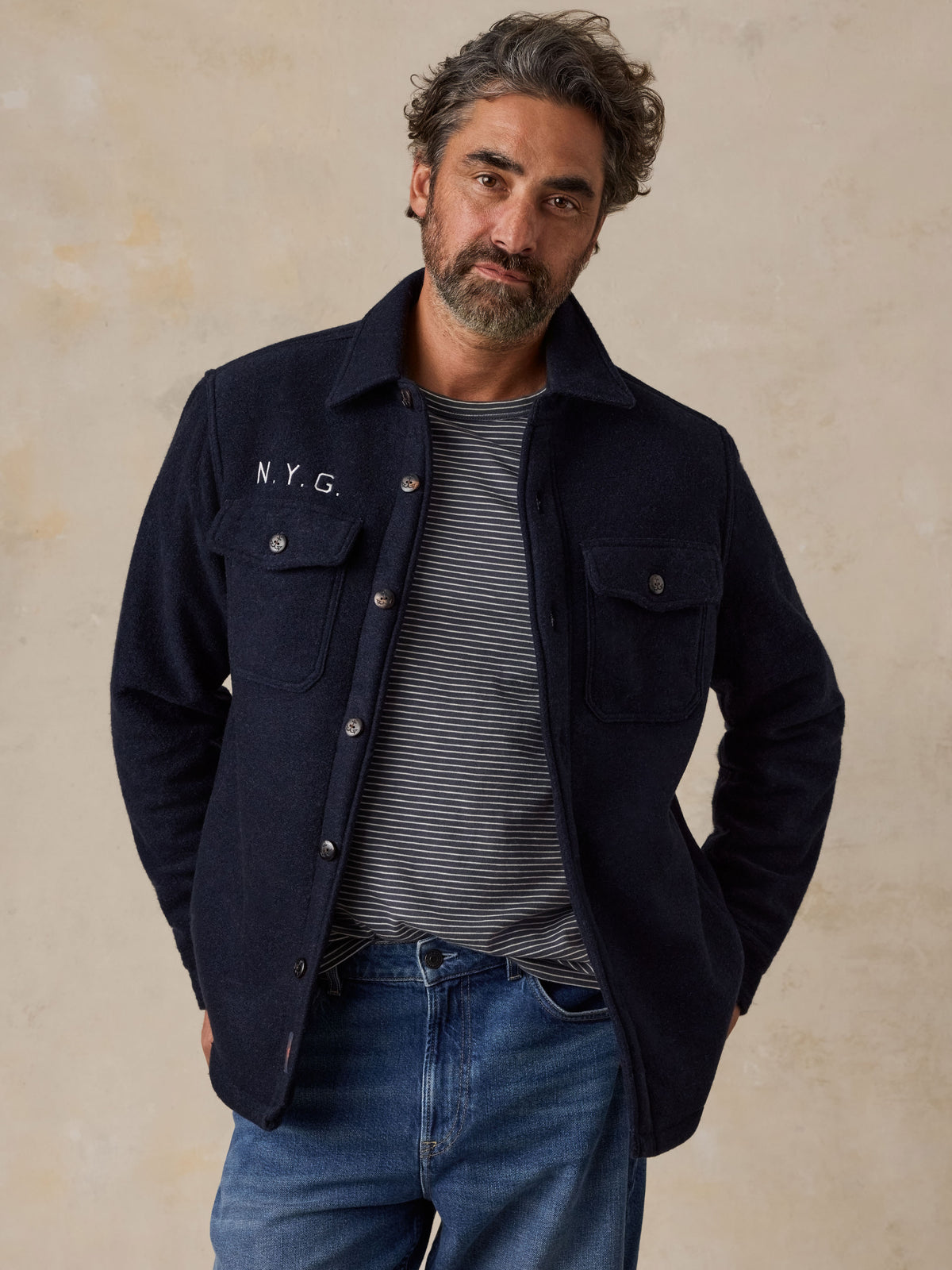 A man wearing a blue NY Giants jacket over a striped tee and blue jeans, image 1 of 5