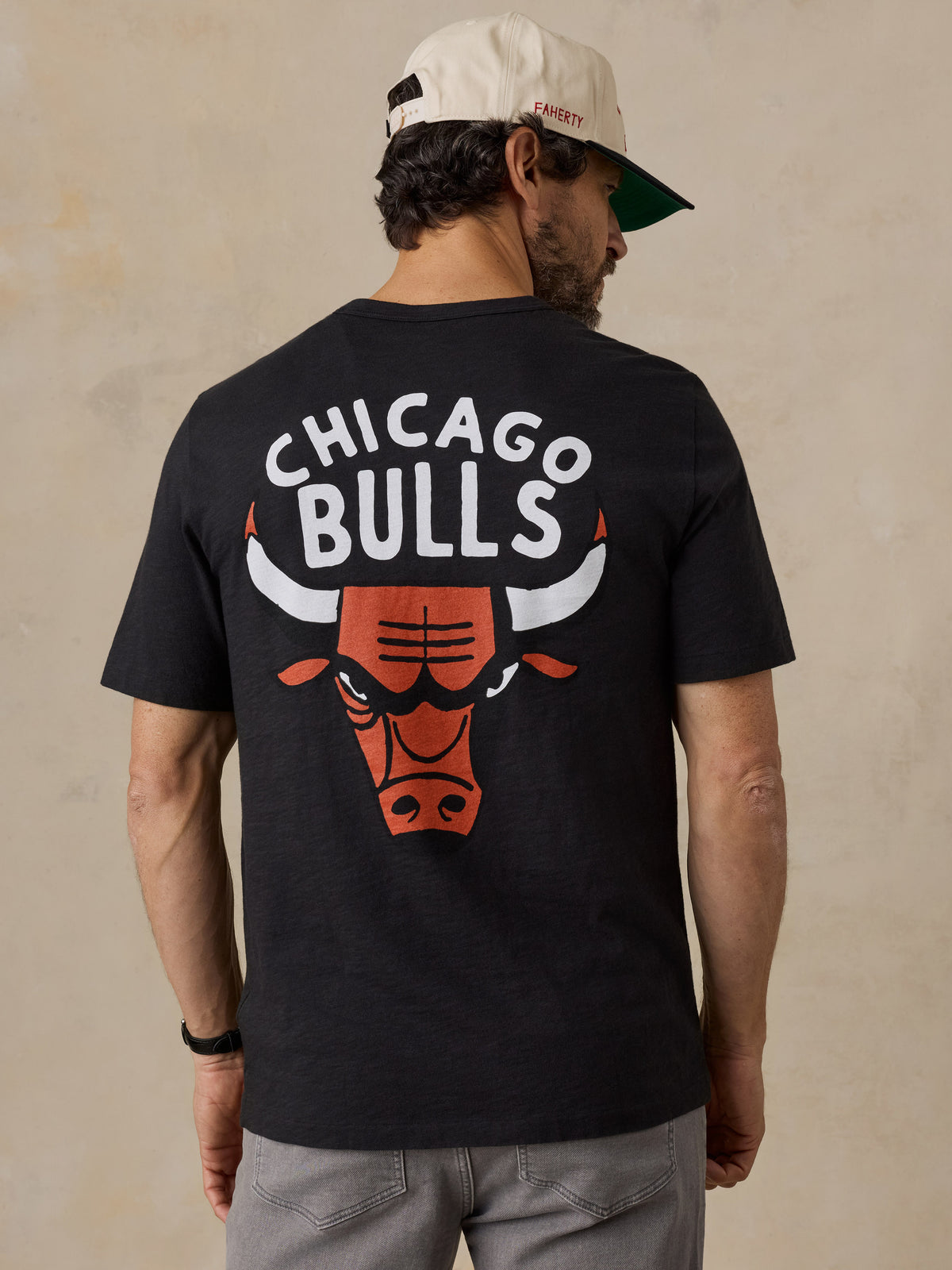 A man viewed from behind wearing a black Chicago bulls tee and hat, image 2 of 6