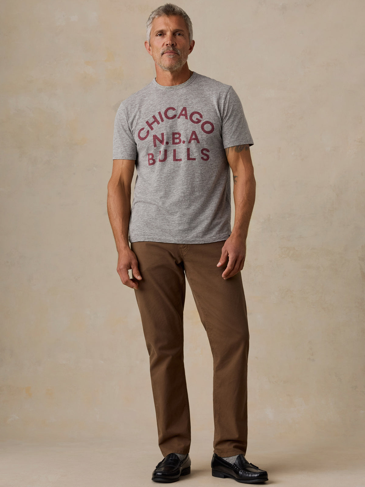 A man wearing a grey Chicago Bulls tee and brown pants, image 5 of 6