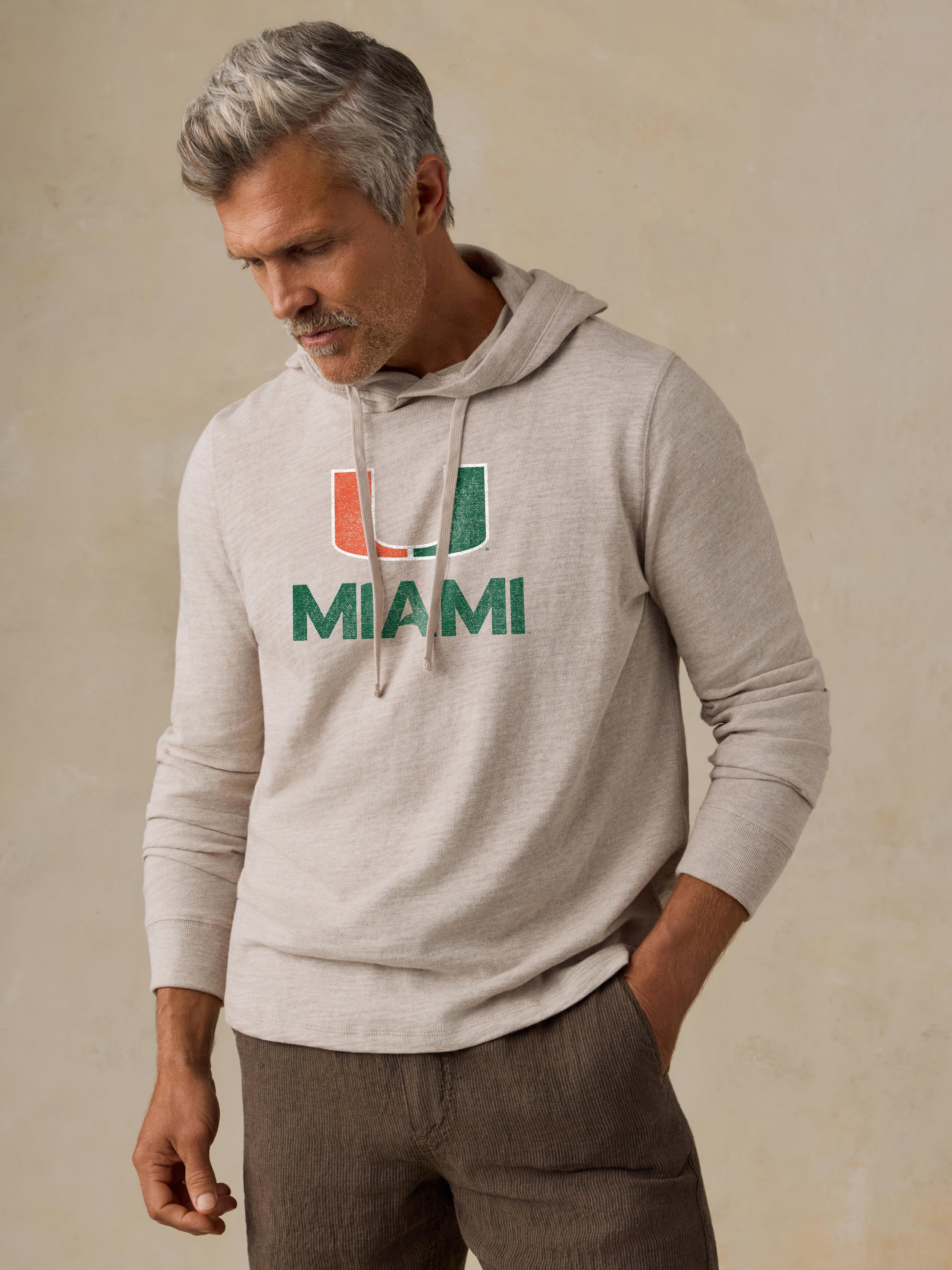 A man wearing a beige University of Miami hoodie and brown shorts
