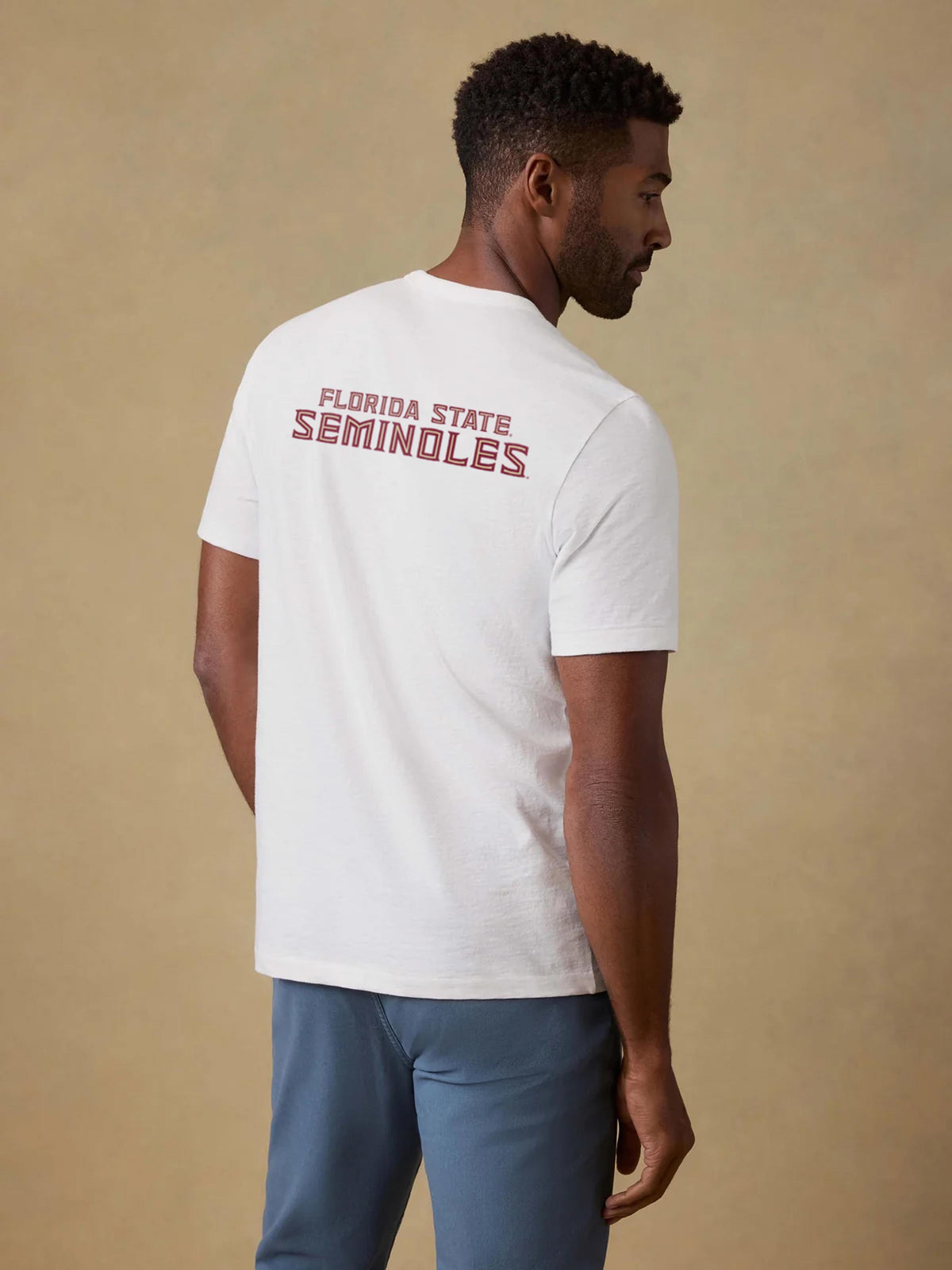 A man viewed from behind wearing a white Florida State pocket tee and blue pants, image 2 of 2