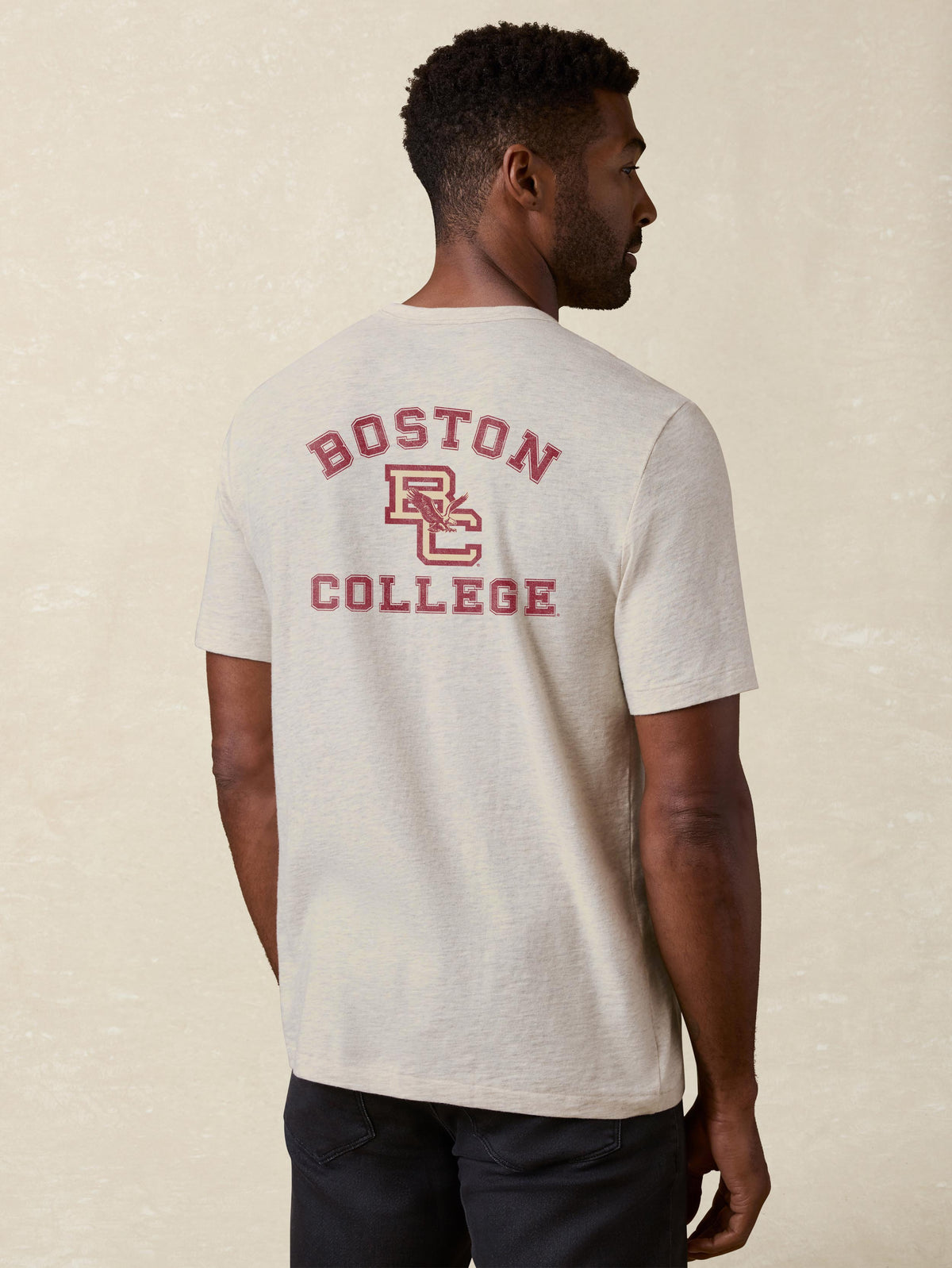 A man viewed from behind wearing a grey Boston College pocket tee and black pants, image 2 of 2
