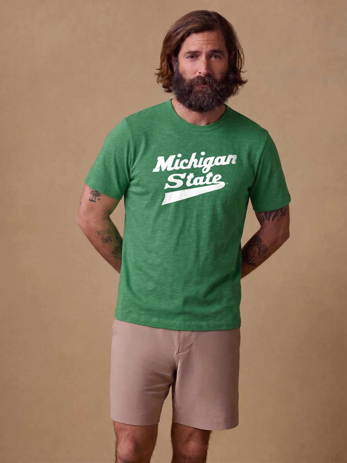 A man wearing a green Michigan State tee and beige shorts, image 1 of 1