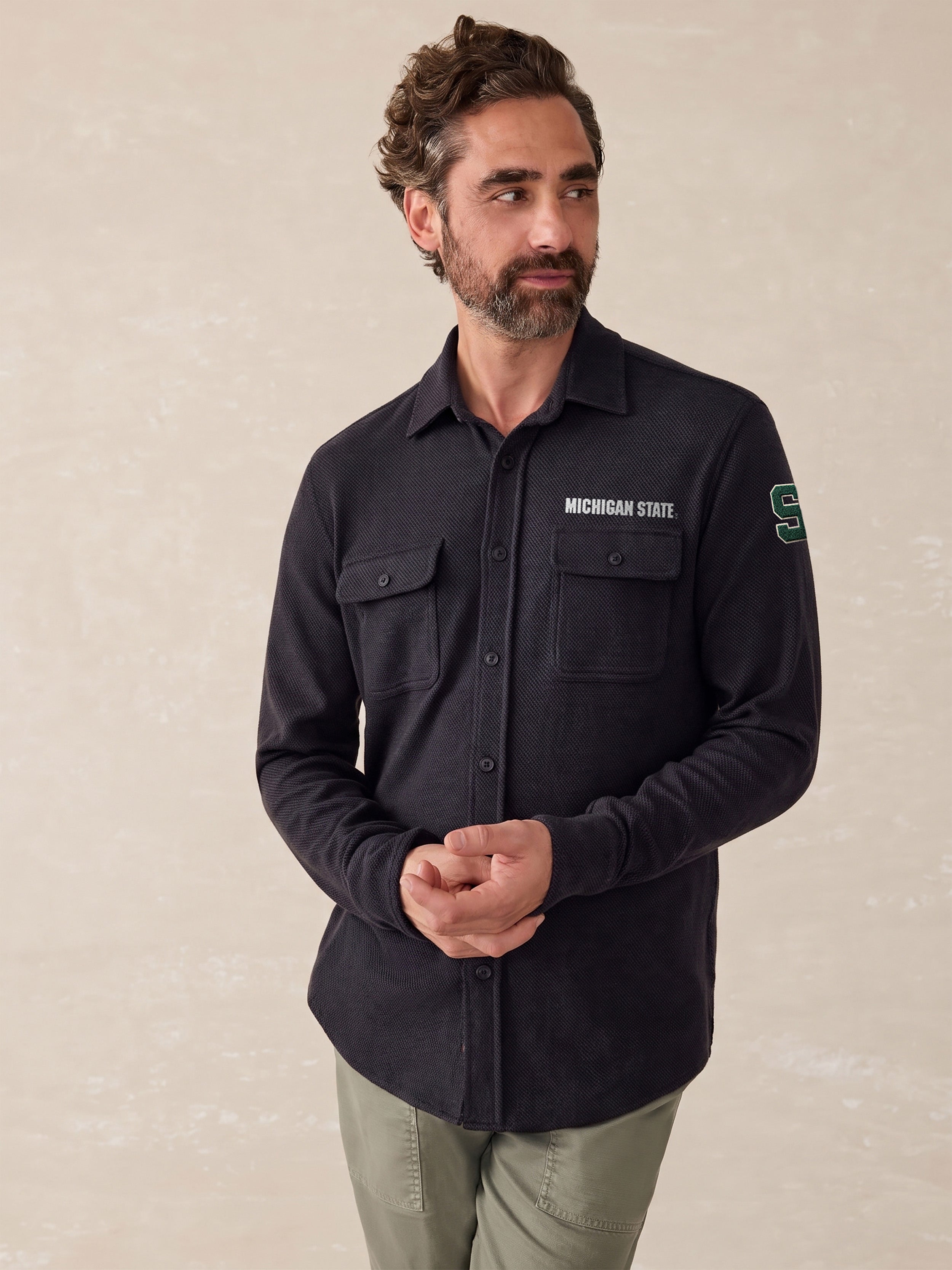 A man wearing a black Michigan State button up shirt and green pants