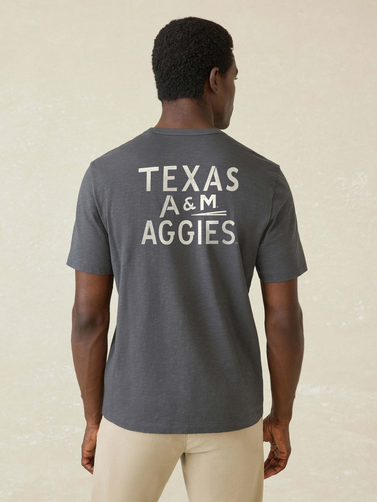 A man viewed from behind wearing a grey Texas A&M tee and beige pants, image 2 of 2