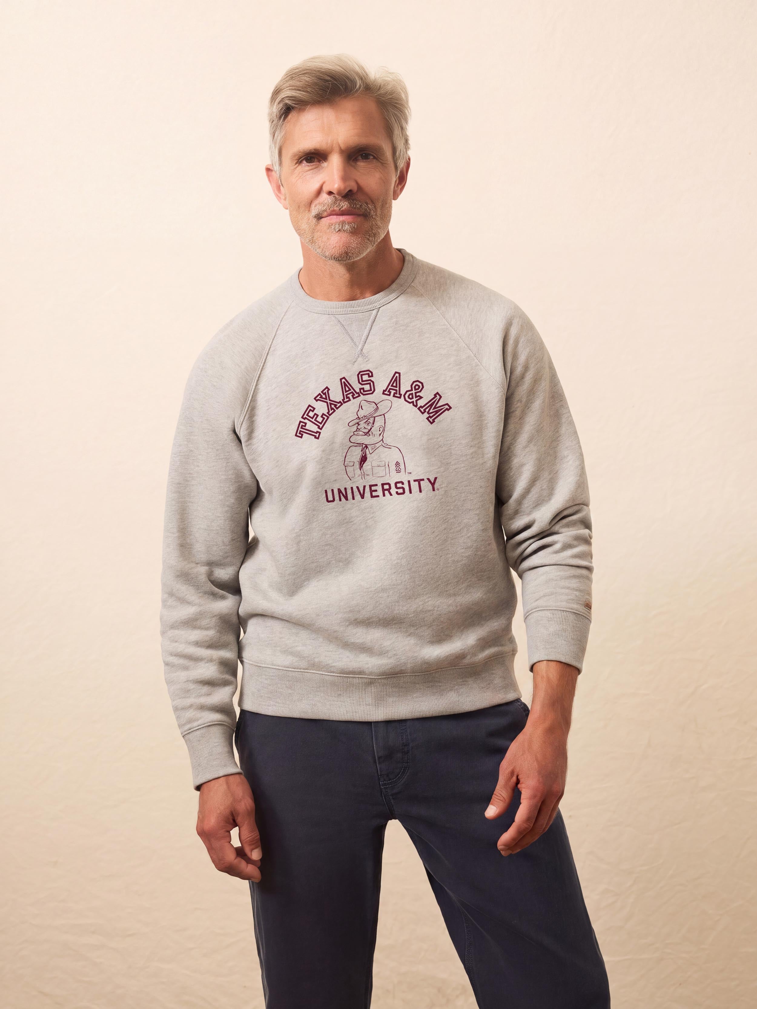A man wearing a grey Texas A&M crewneck and blue pants