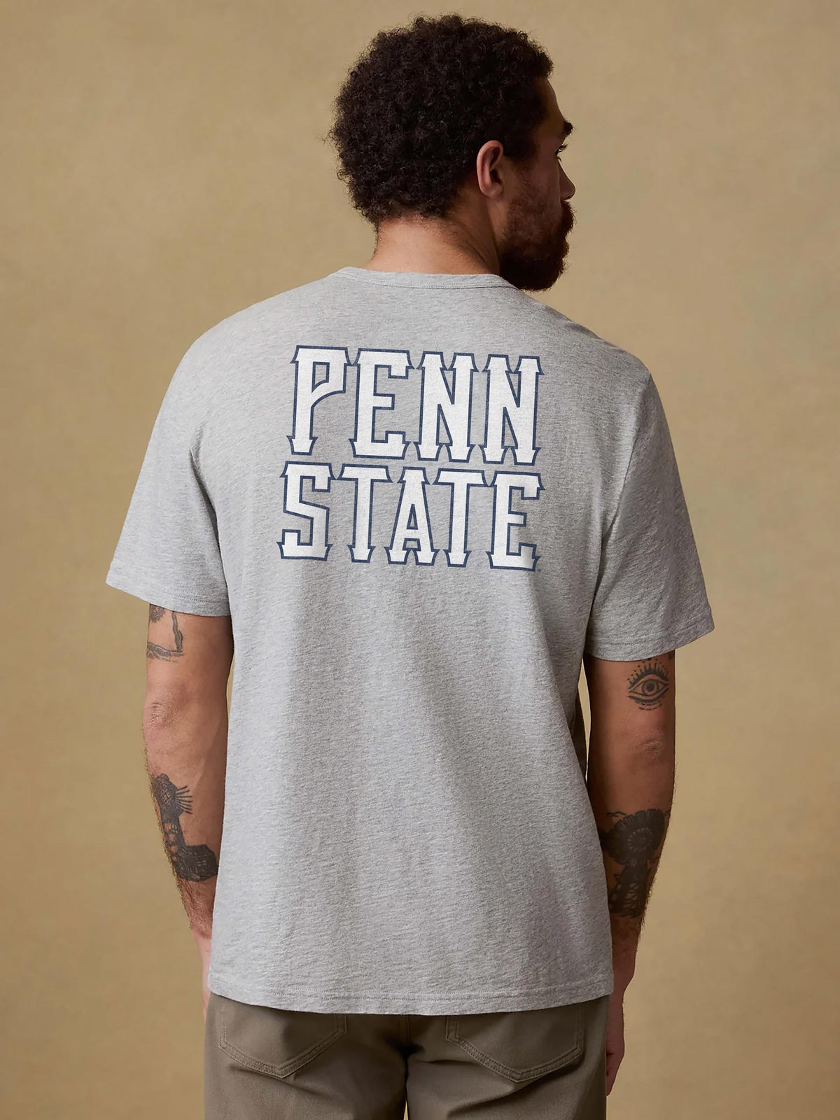 A man viewed from behind wearing a grey Penn State tee and brown pants, image 2 of 2