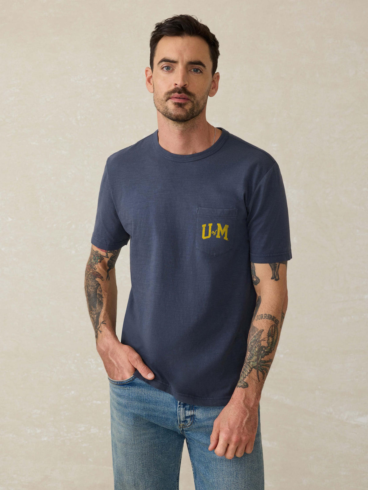 A man wearing a blue University of Michigan tee and blue jeans, image 1 of 2