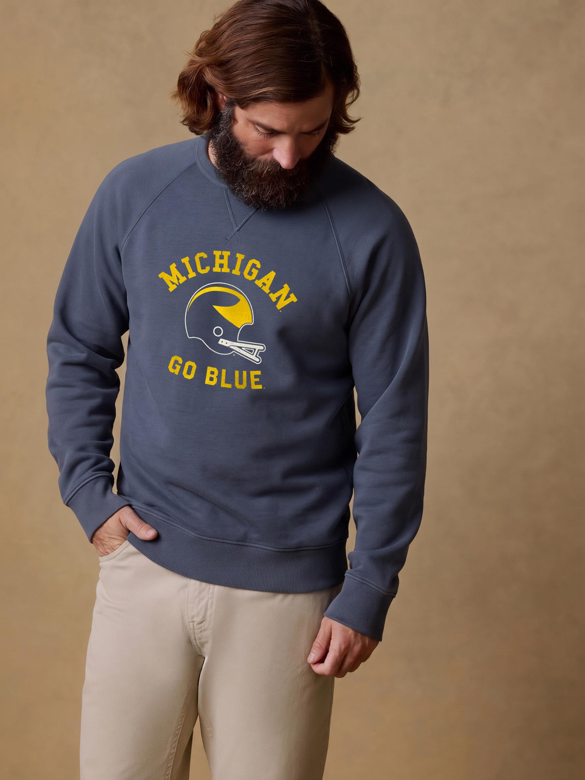 A man wearing a blue University of Michigan crewneck and beige pants, image 1 of 1