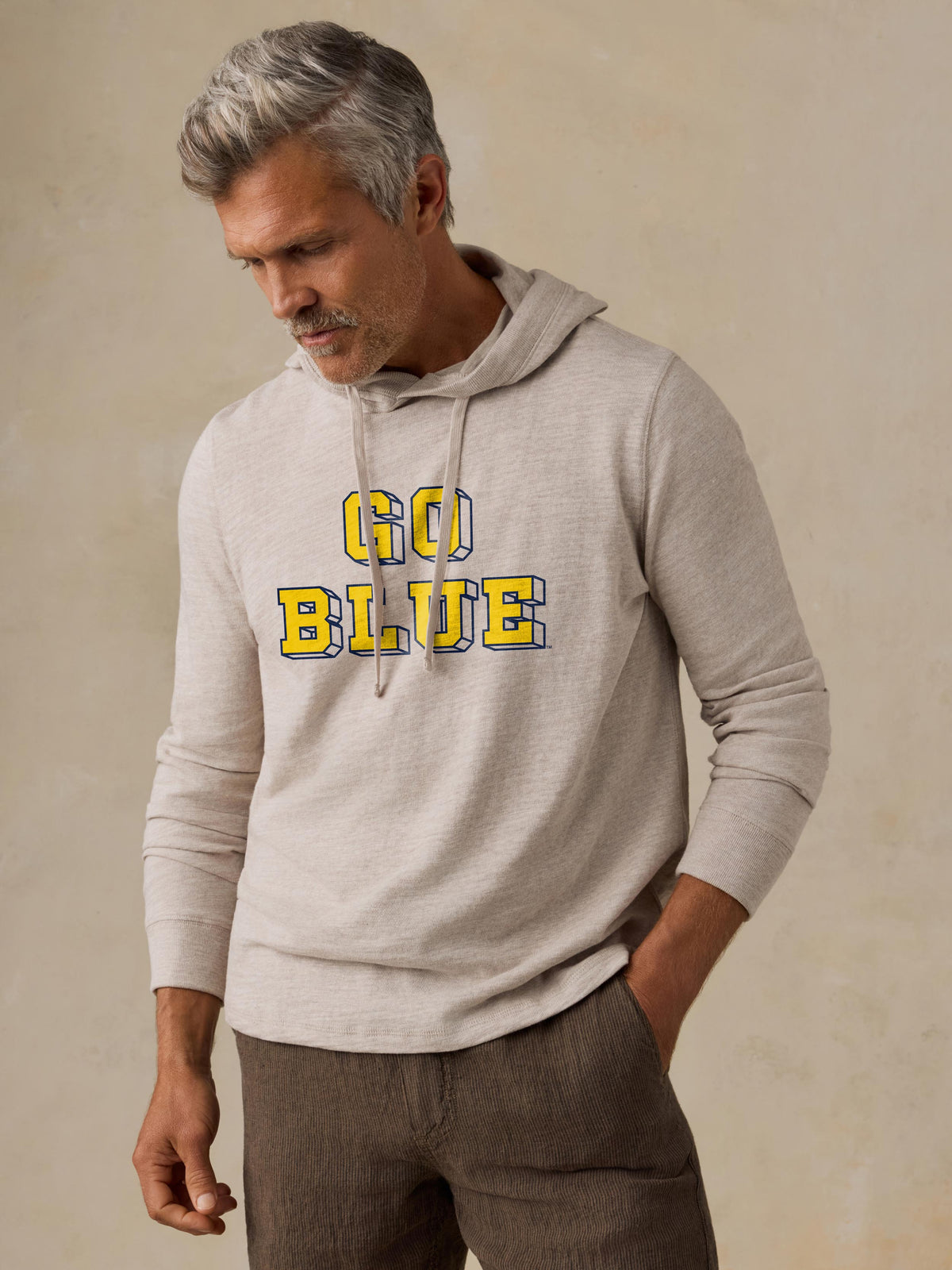 A man wearing a grey University of Michigan hoodie and brown shorts, image 1 of 1