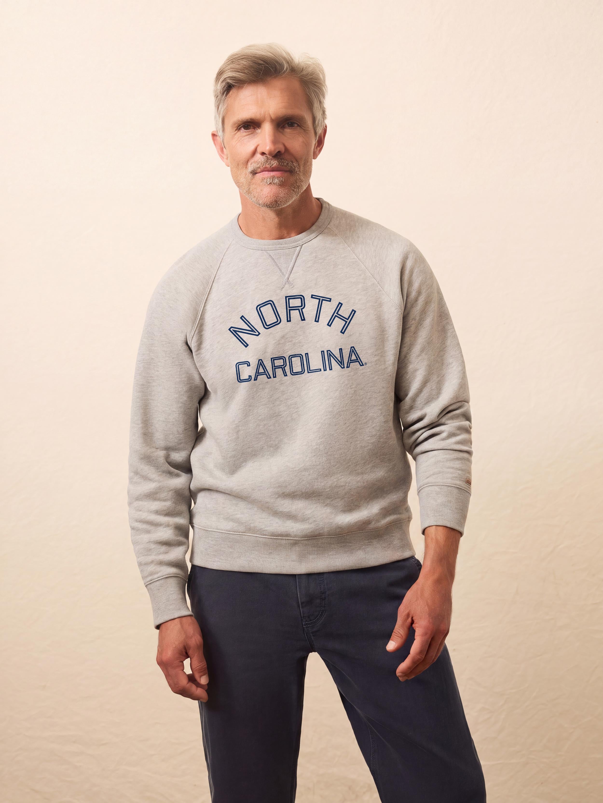 A man wearing a grey University of North Carolina crewneck and blue pants