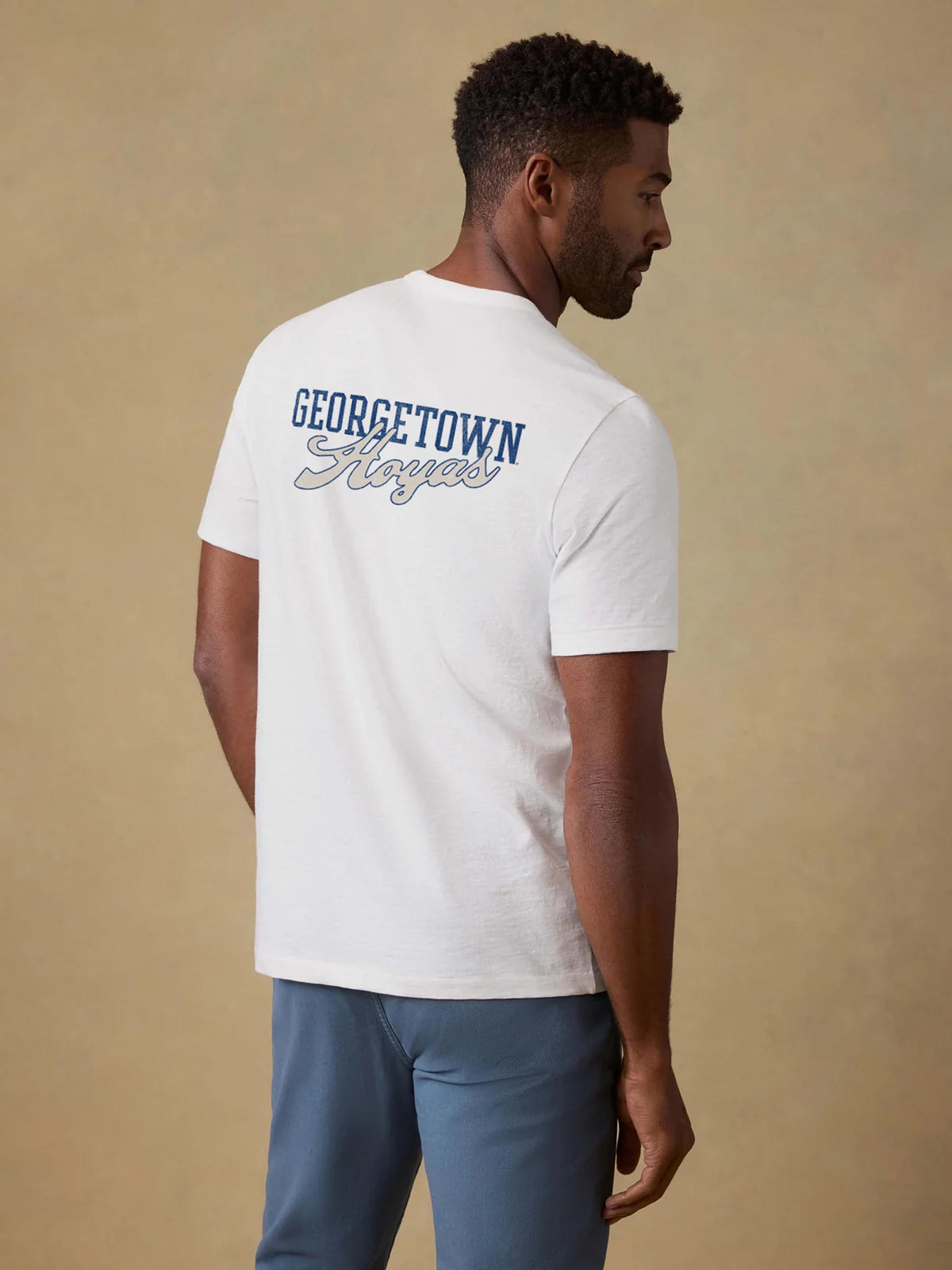 A man viewed from behind wearing a white Georgetown tee and blue pants, image 2 of 2