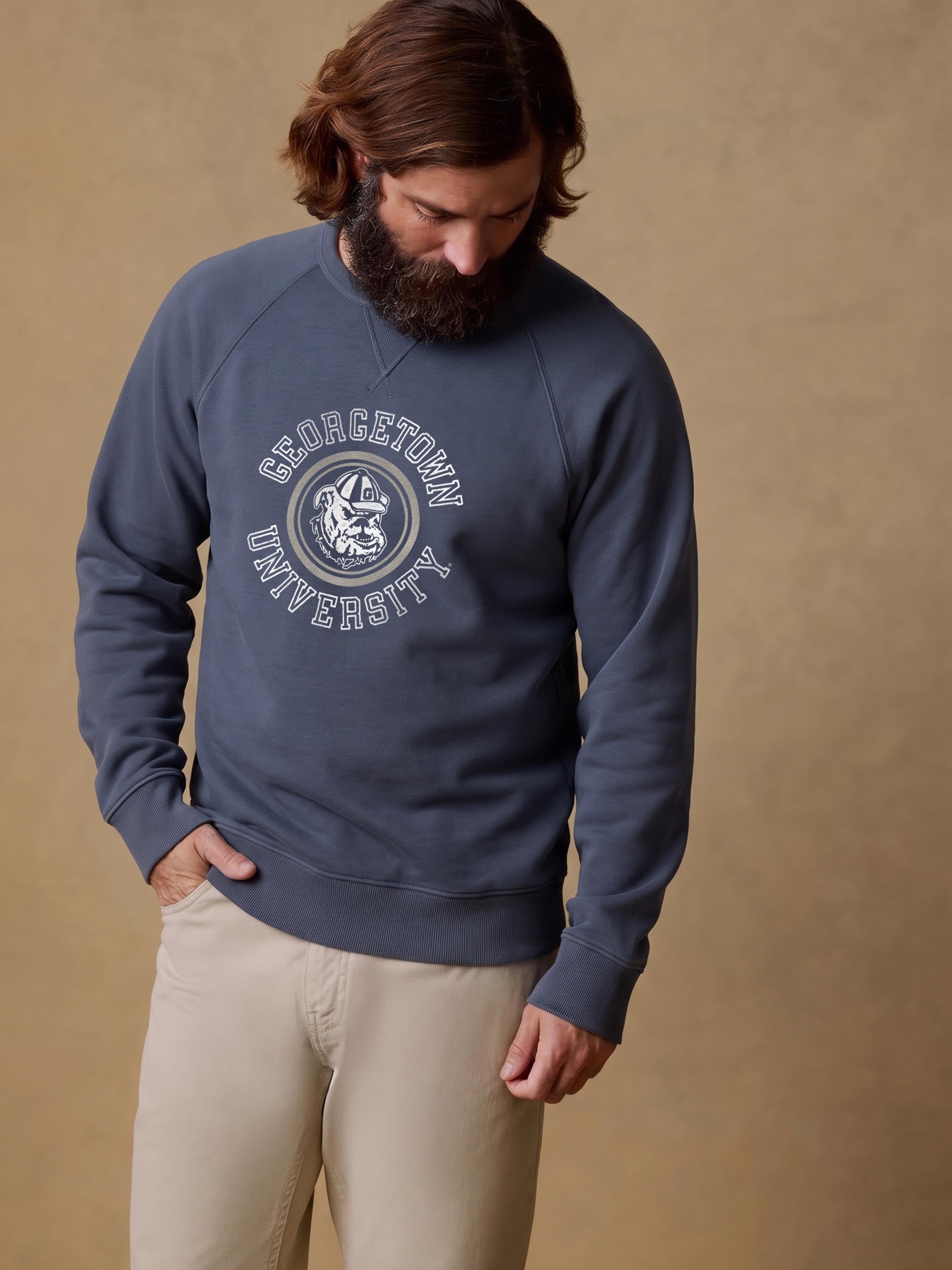 A man wearing a blue Georgetown crewneck and beige pants