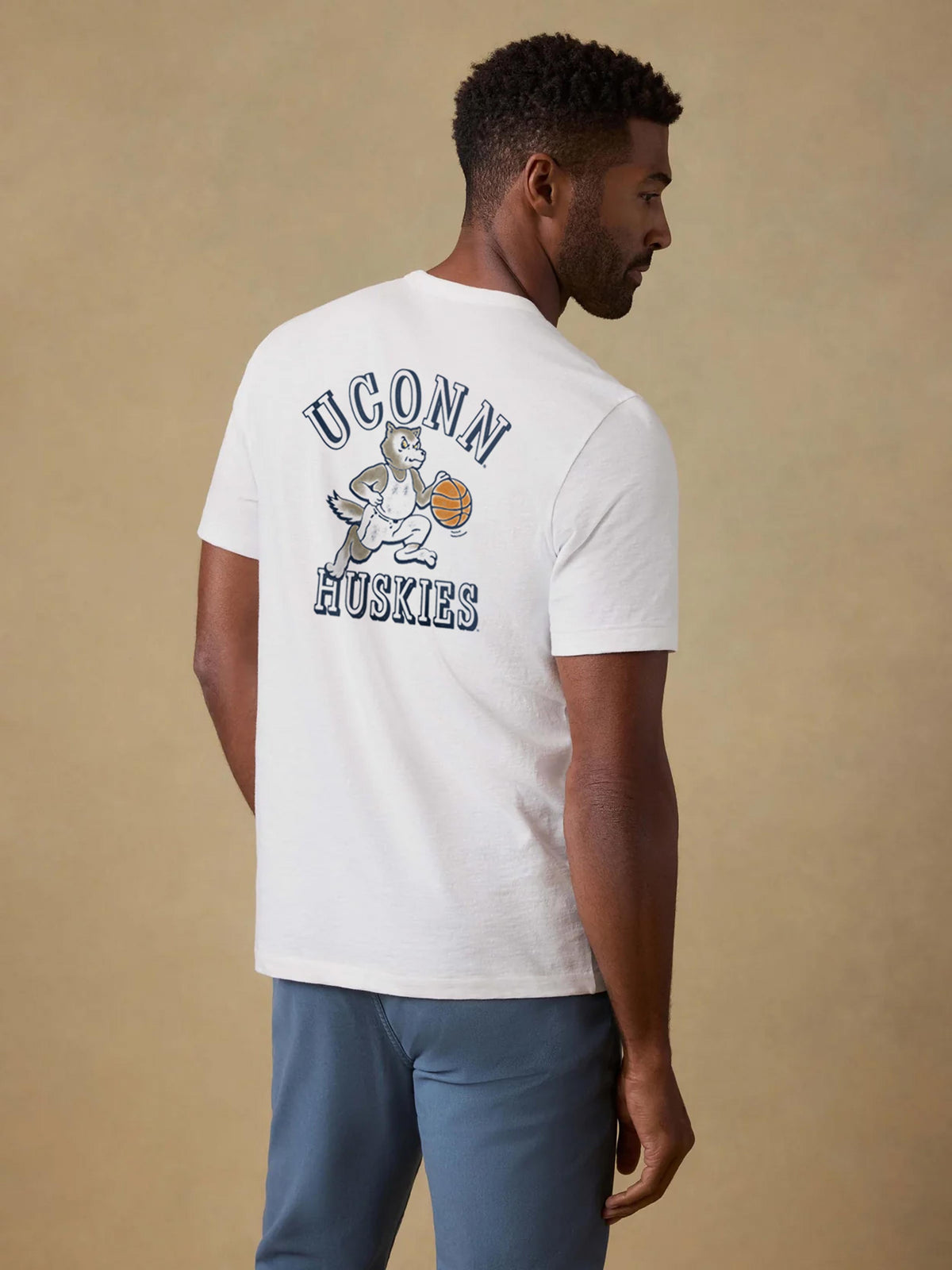 A man viewed from behind wearing a white UCONN tee and blue pants, image 2 of 2