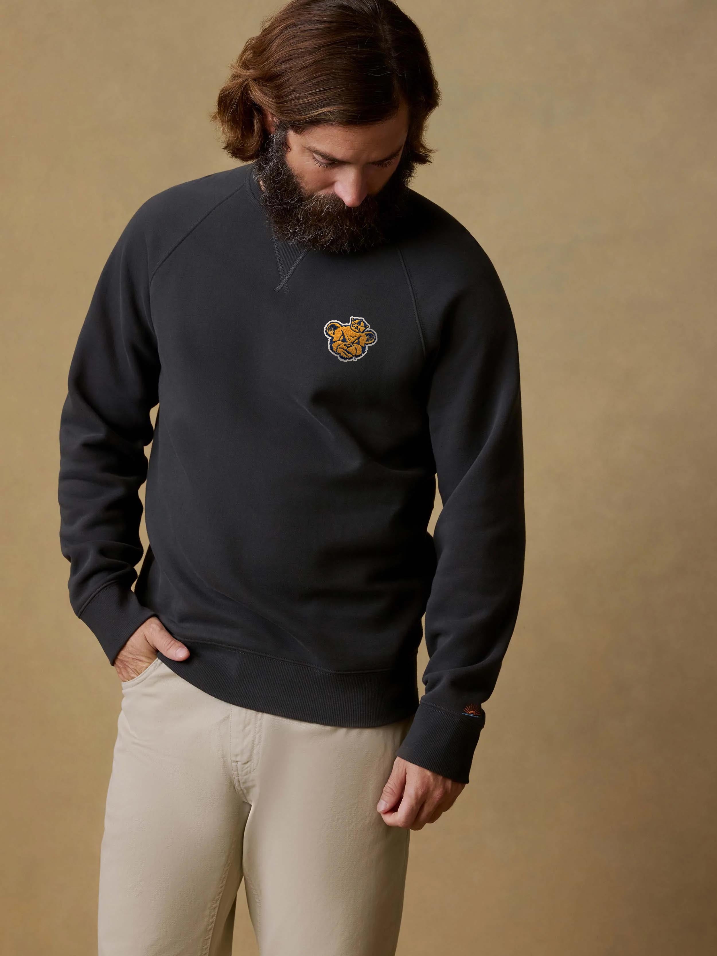 A man wearing a black UC Berkeley crewneck and beige pants