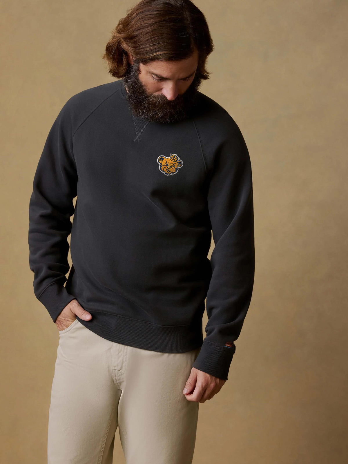 A man wearing a black UC Berkeley crewneck and beige pants, image 1 of 1