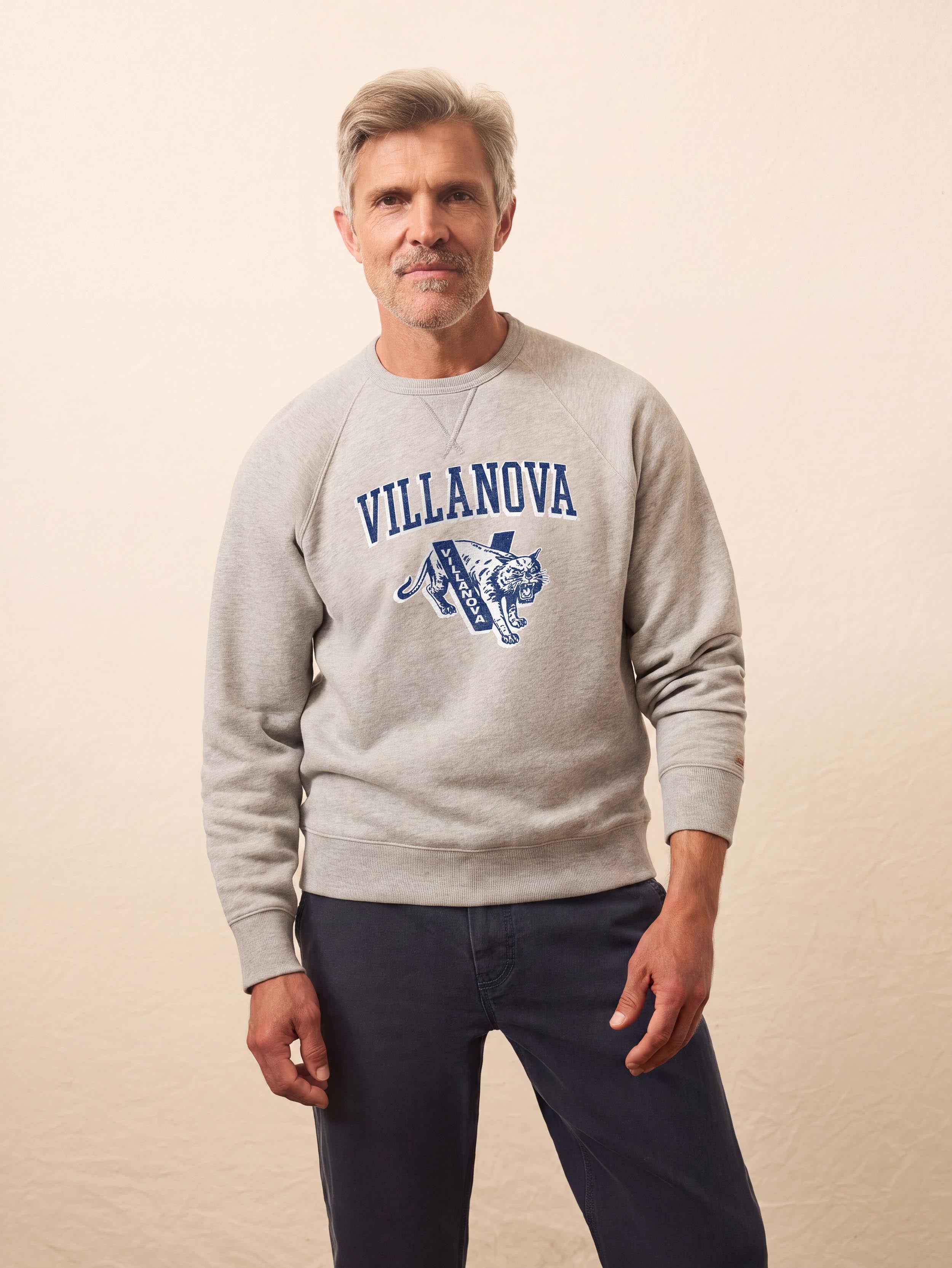 A man wearing a grey Villanova crewneck and blue pants