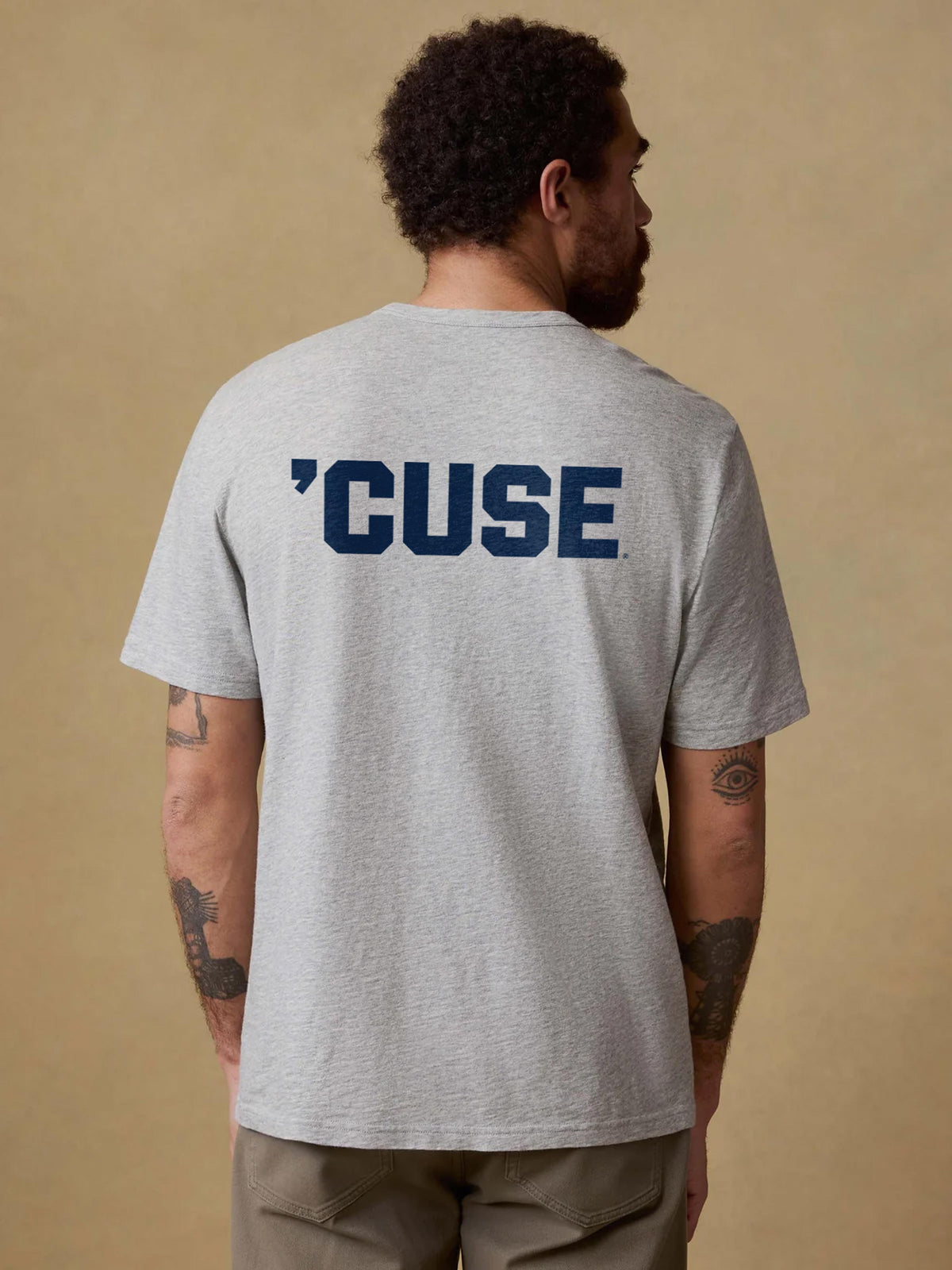 A man viewed from behind wearing a grey Syracuse pocket tee and brown pants, image 2 of 2