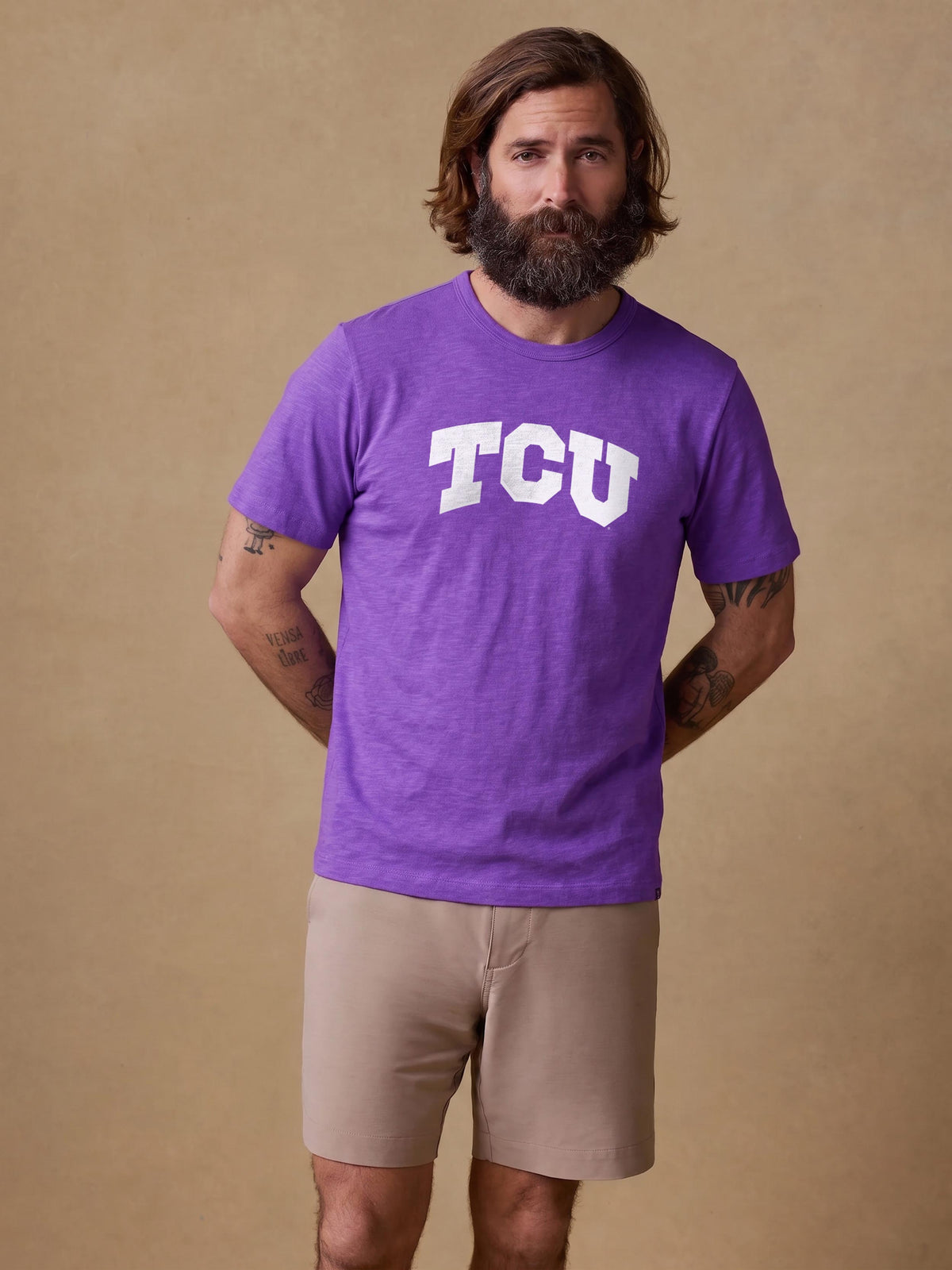 A man wearing a purple TCU tee and beige shorts, image 1 of 1