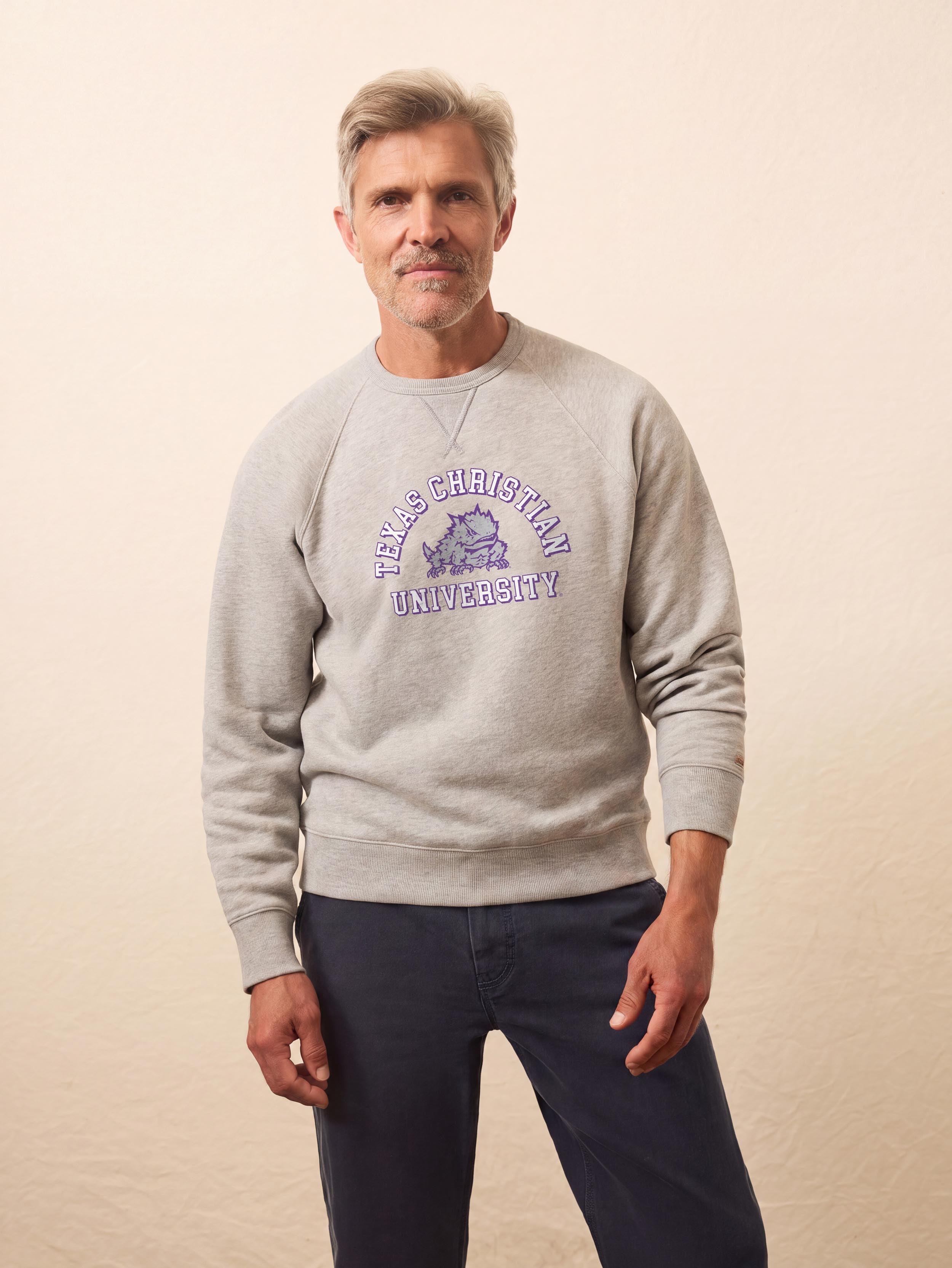 A man wearing a grey TCU crewneck and blue pants