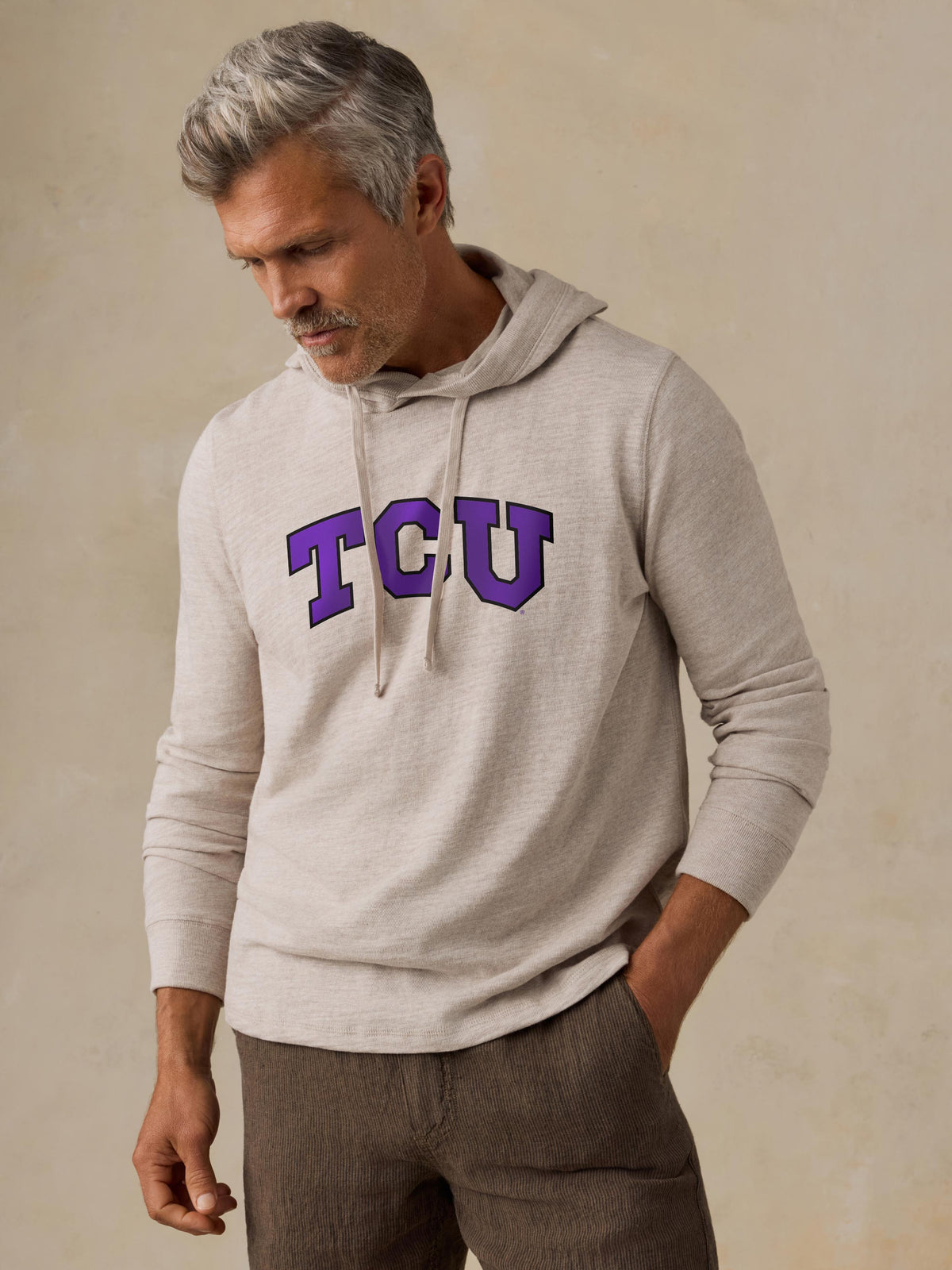 A man wearing a beige TCU hoodie and brown shorts, image 1 of 1