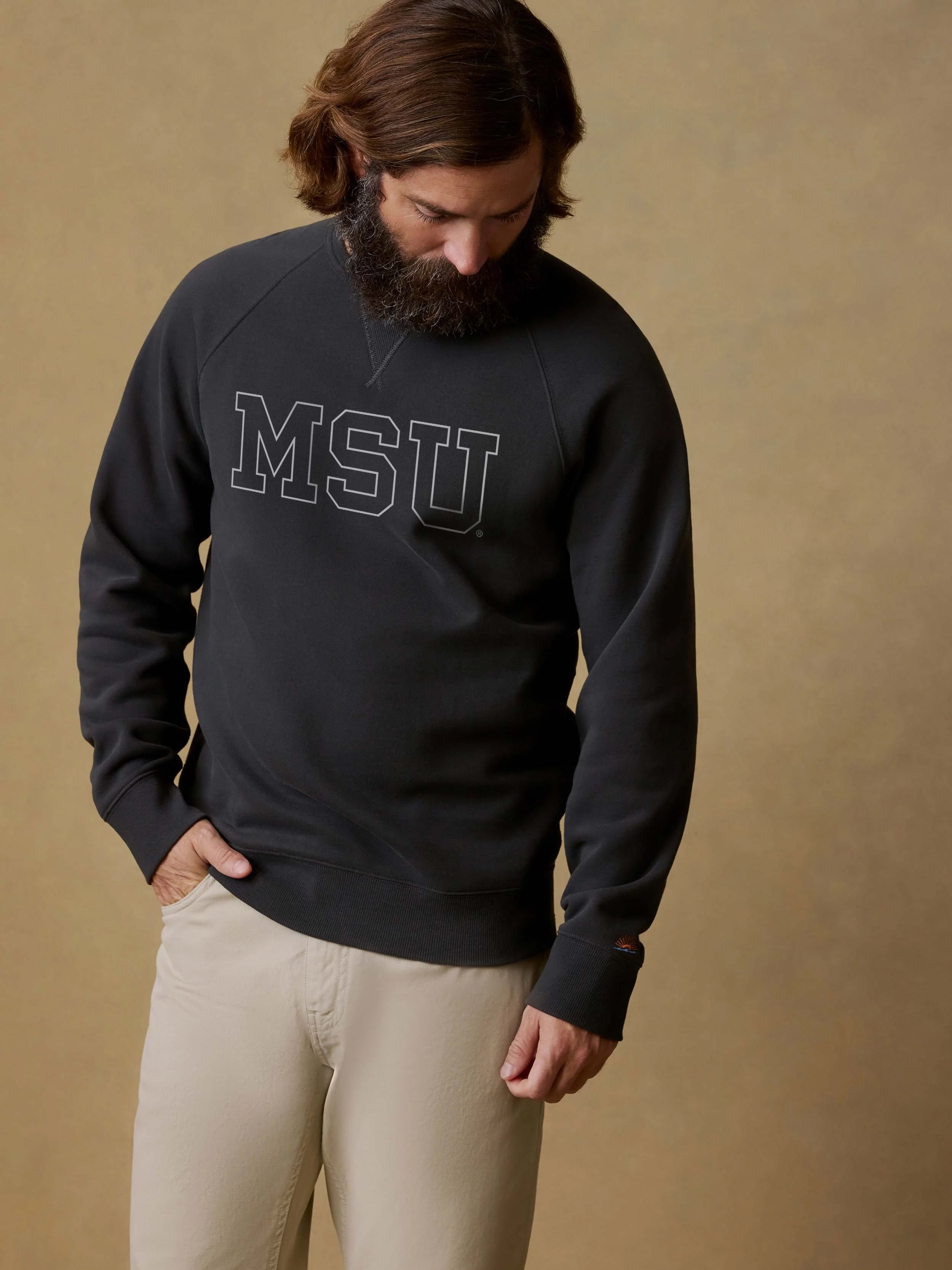 Man wearing a black sweatshirt with MSU text on the center front against a beige background