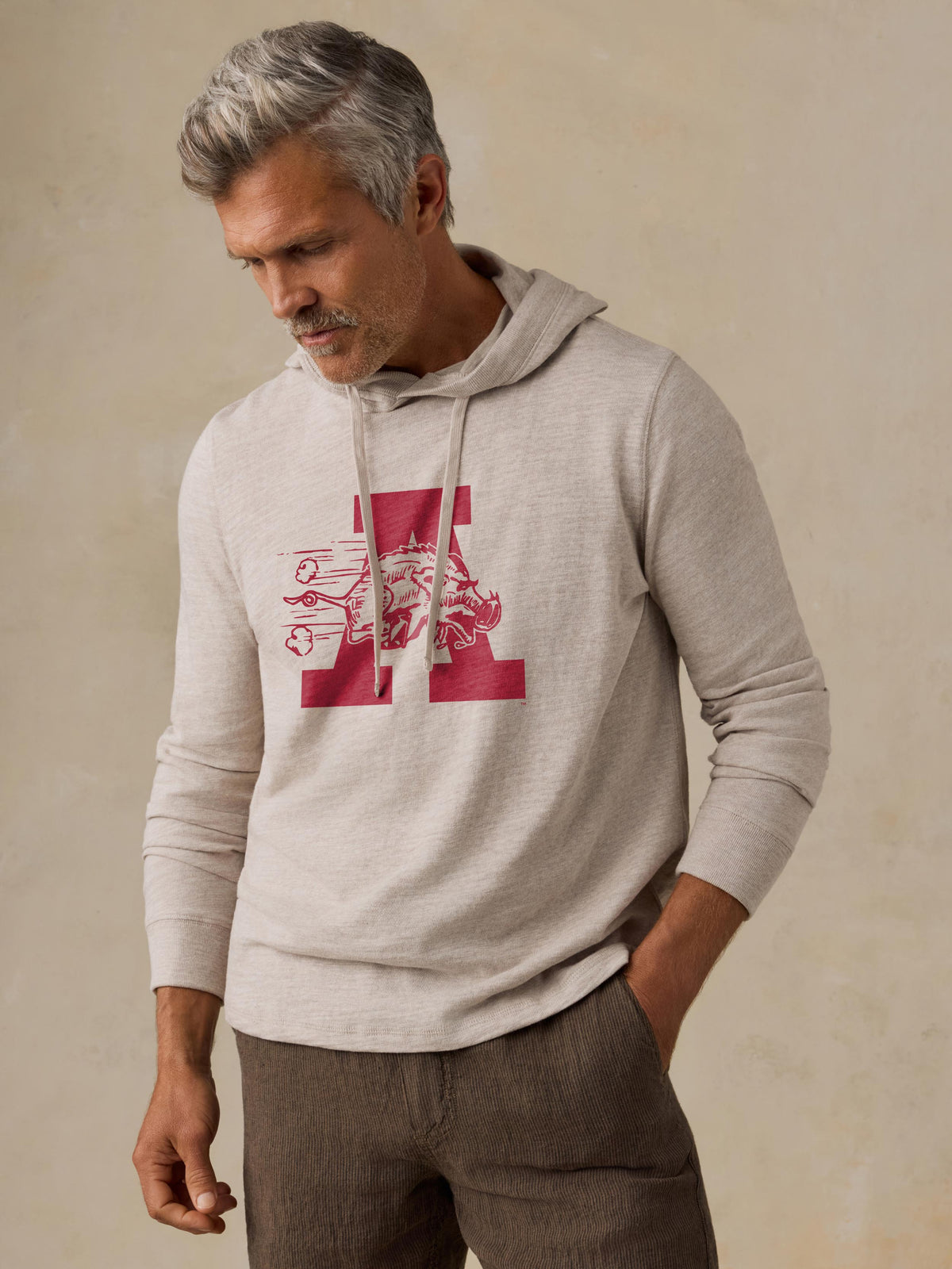 A man is wearing a beige University of Arkansas hoodie and brown shorts, image 1 of 1