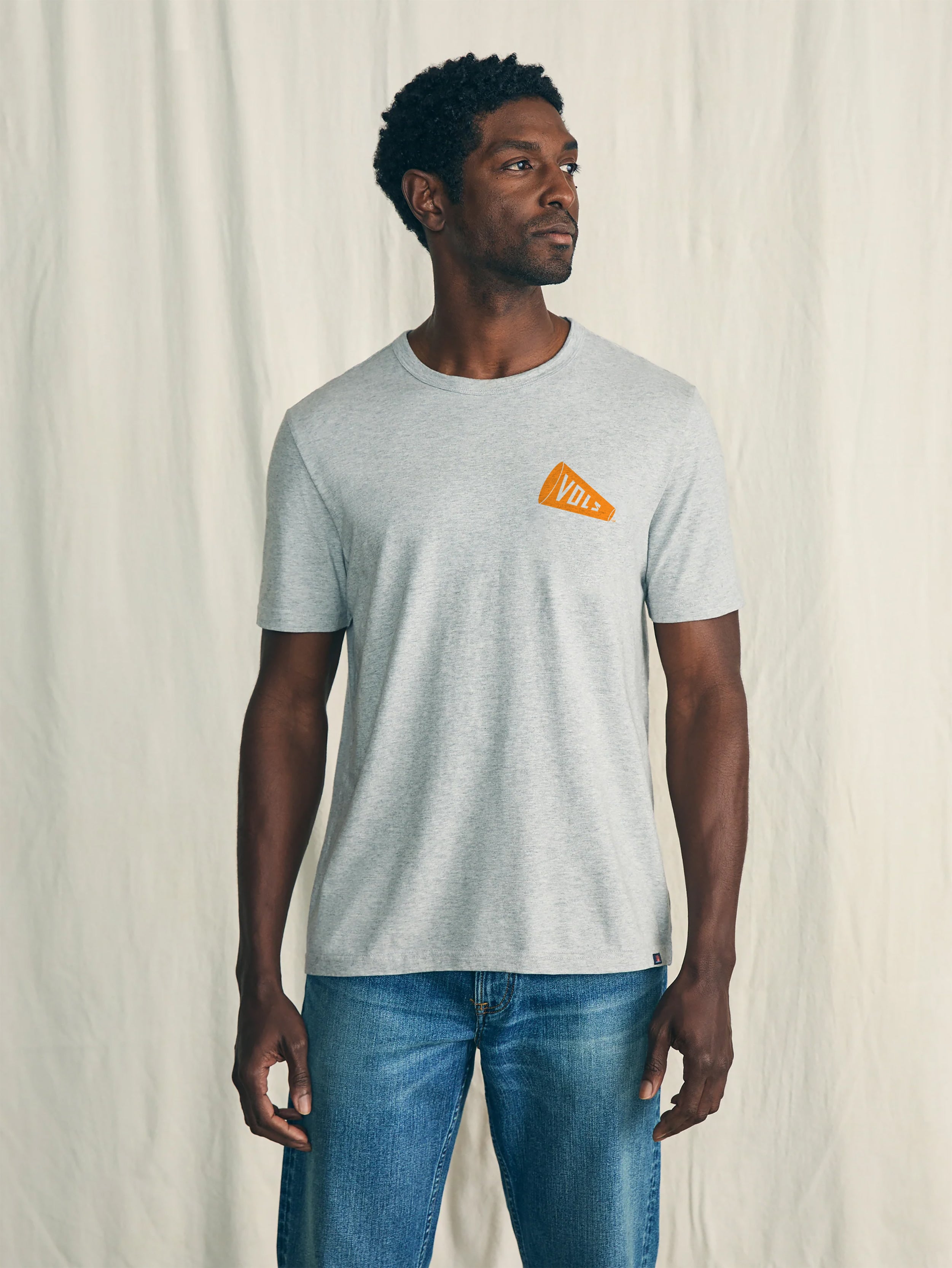 Man wearing a gray t-shirt with a University of Tennessee graphic on the left chest against a plain background