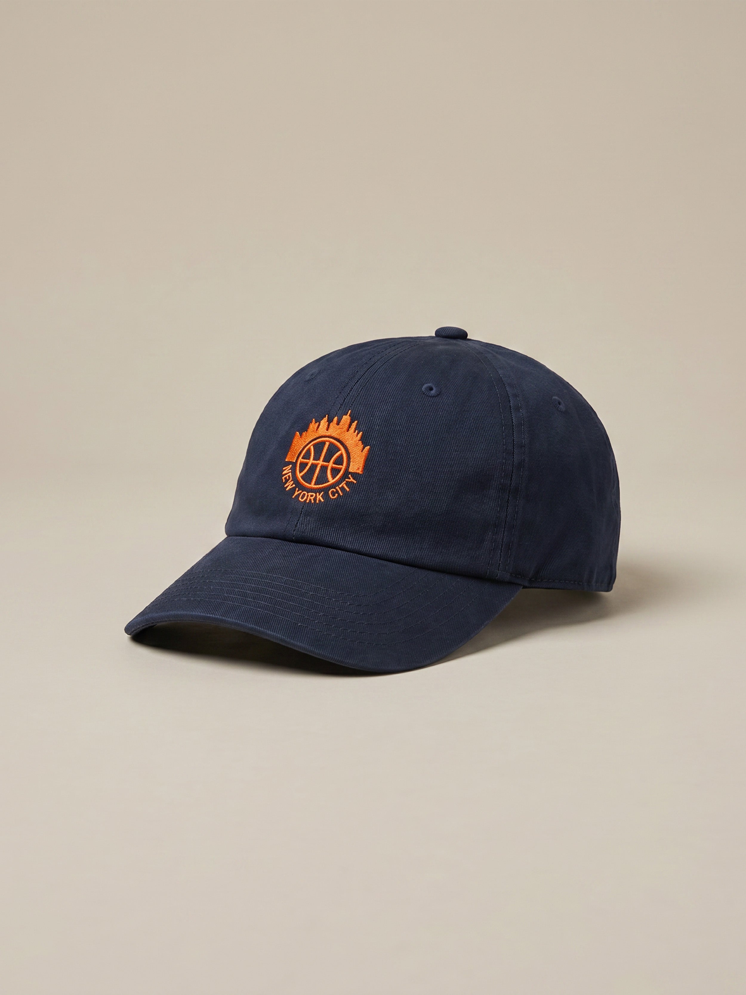 Navy blue cap with orange Jalen Brunson graphic logo against a beige background