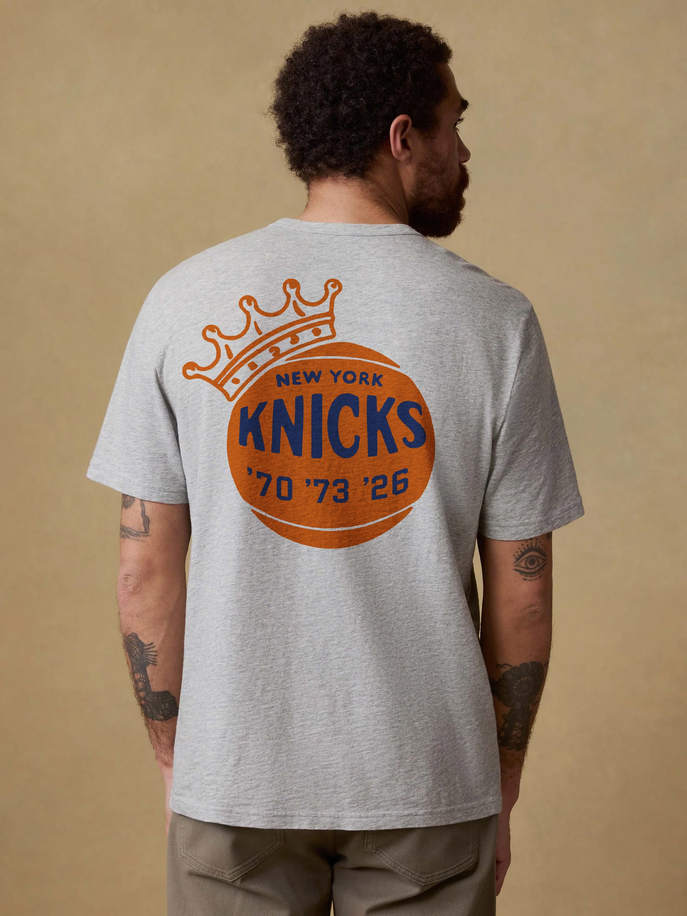 Man wearing a gray t-shirt with New York Knicks graphic on the back against a beige background