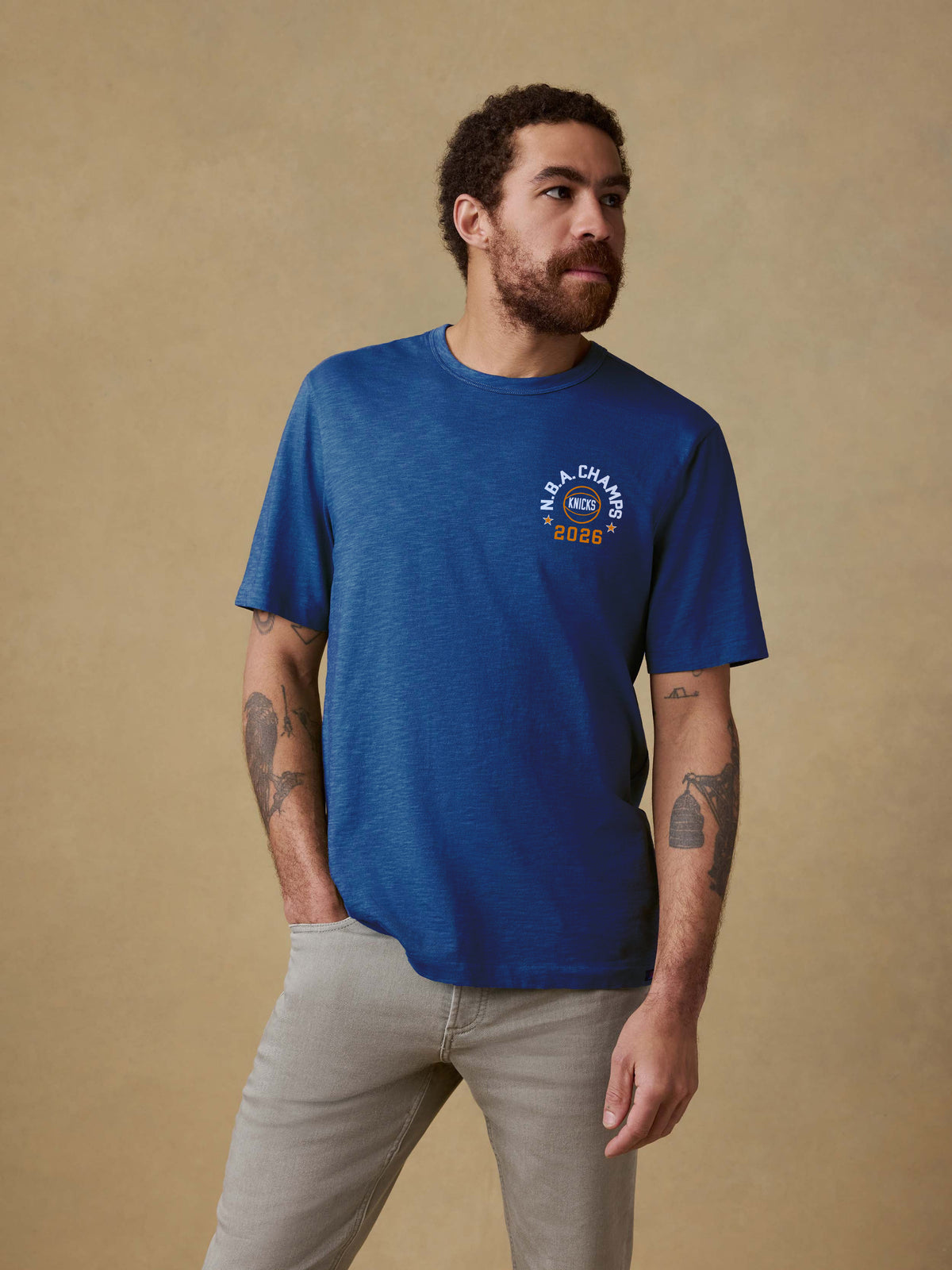 Man wearing a blue t-shirt with NY Knicks NBA Champs graphic on the left chest against a beige background