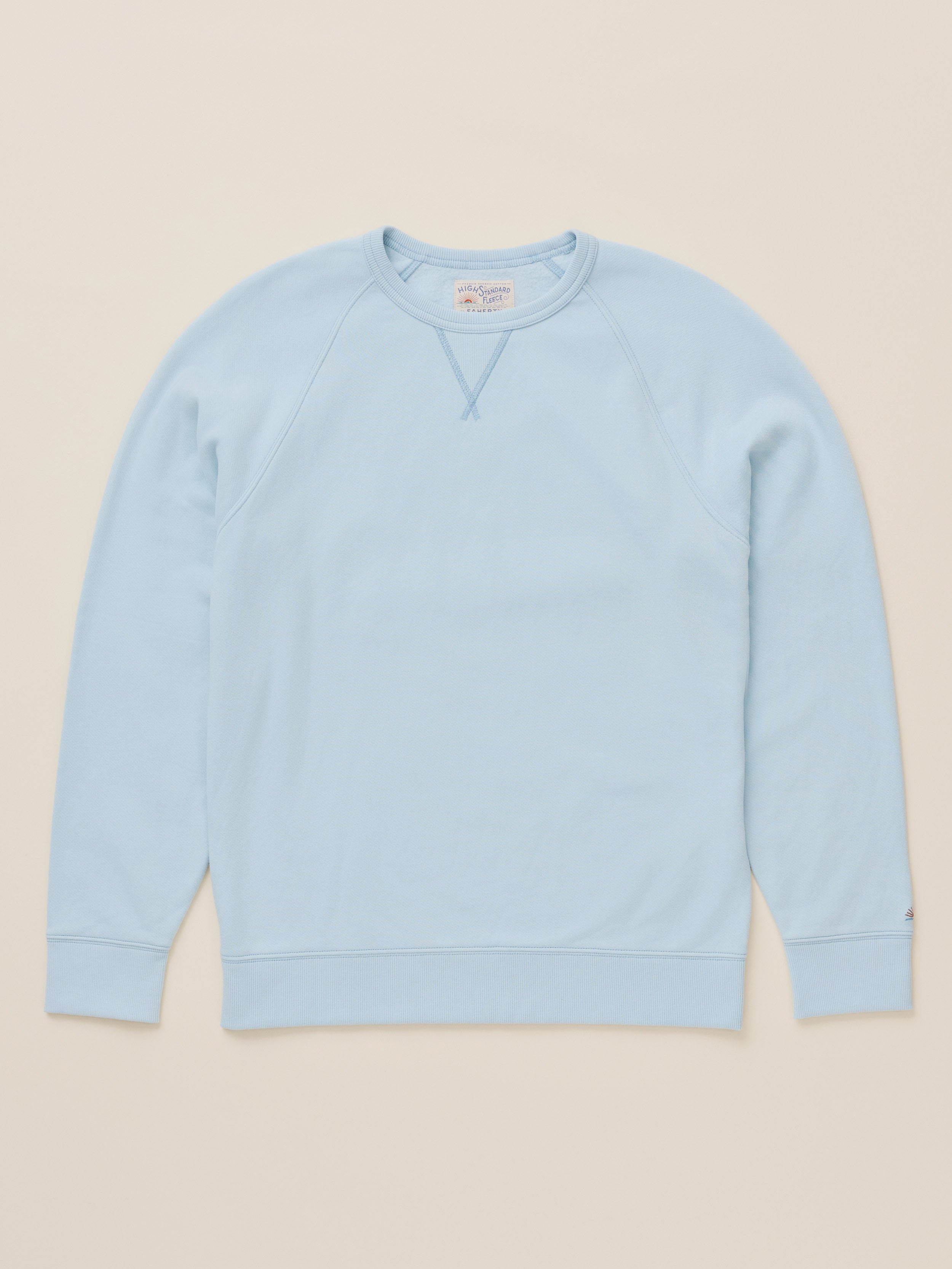 A light blue crewneck sweatshirt with raglan sleeves, laid flat against a solid beige background.