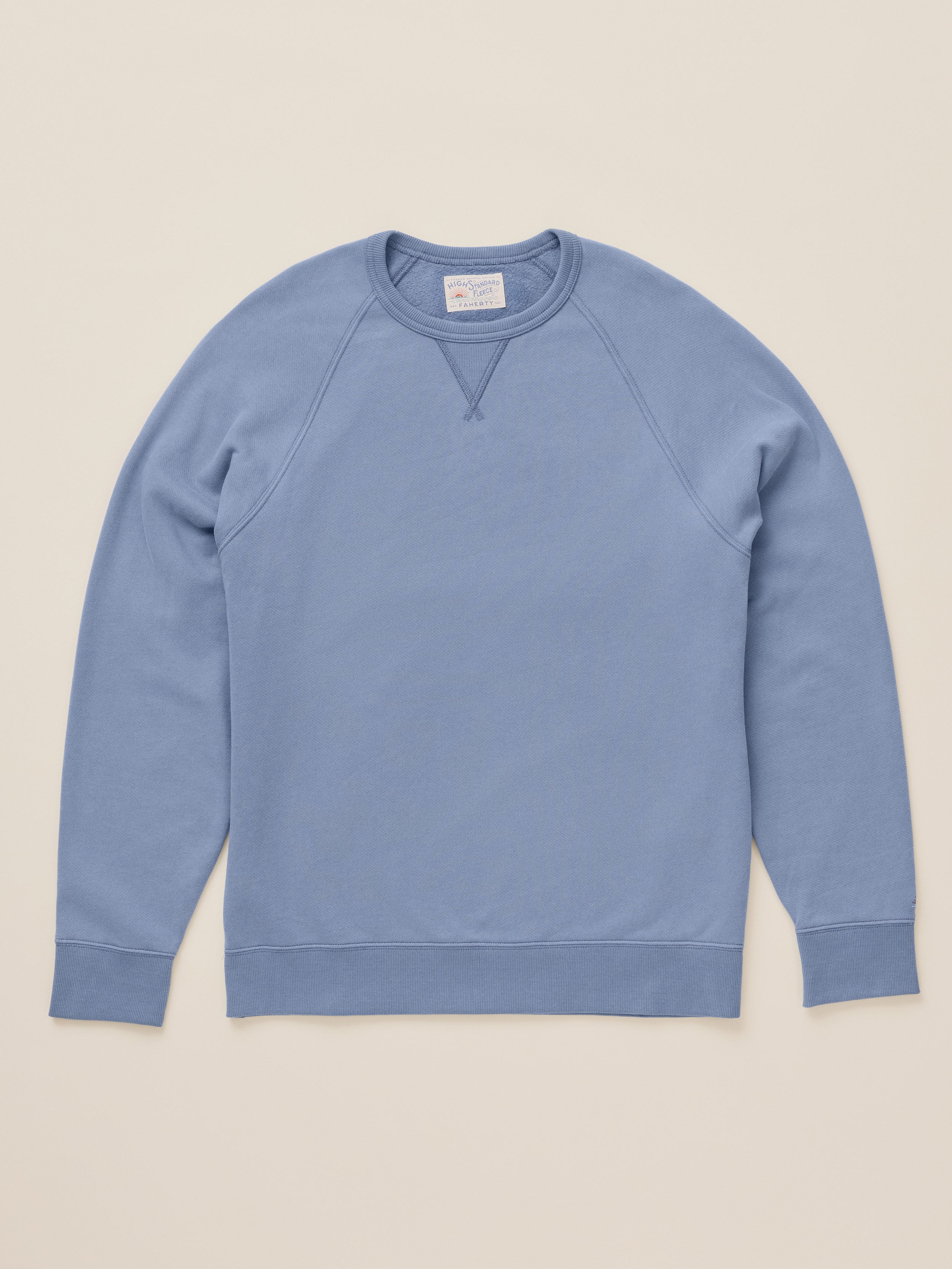 A light blue ribbed crewneck sweatshirt laid flat against a solid beige background.