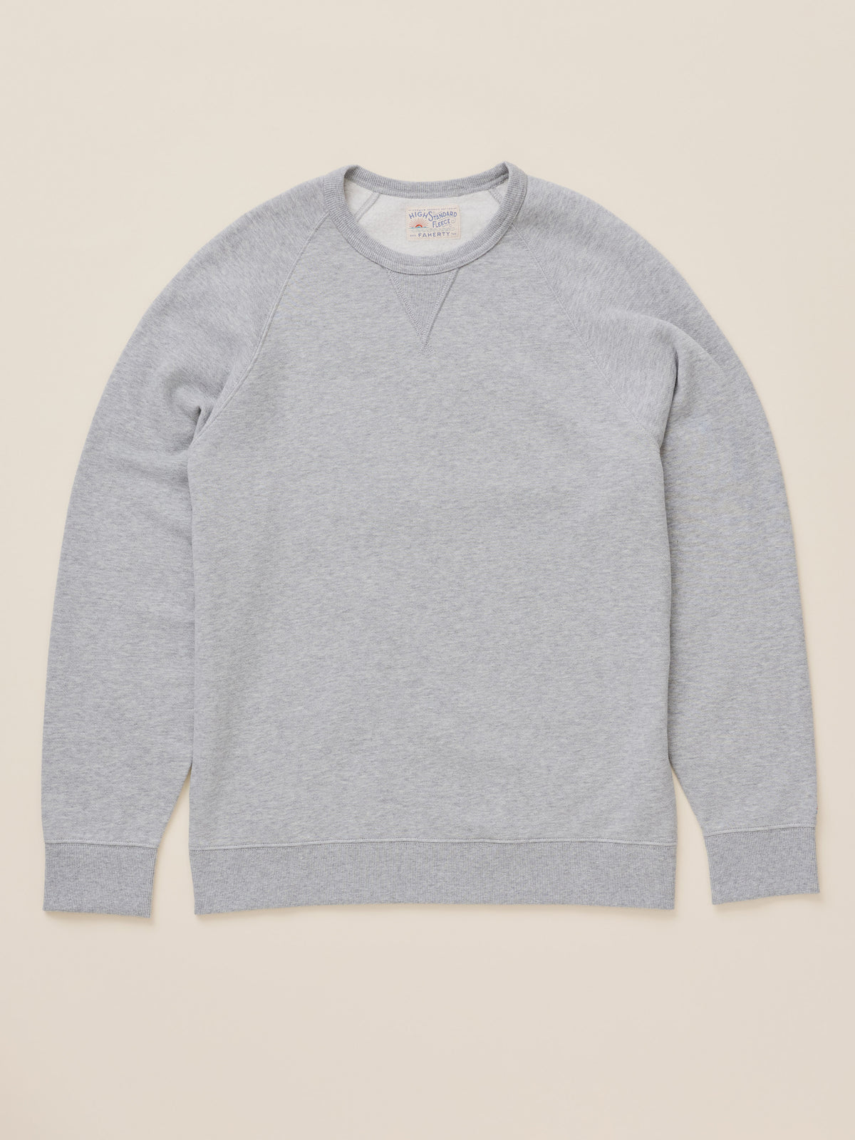 A light gray heather crewneck sweatshirt with raglan sleeves, laid flat against a solid beige background., image 1 of 2