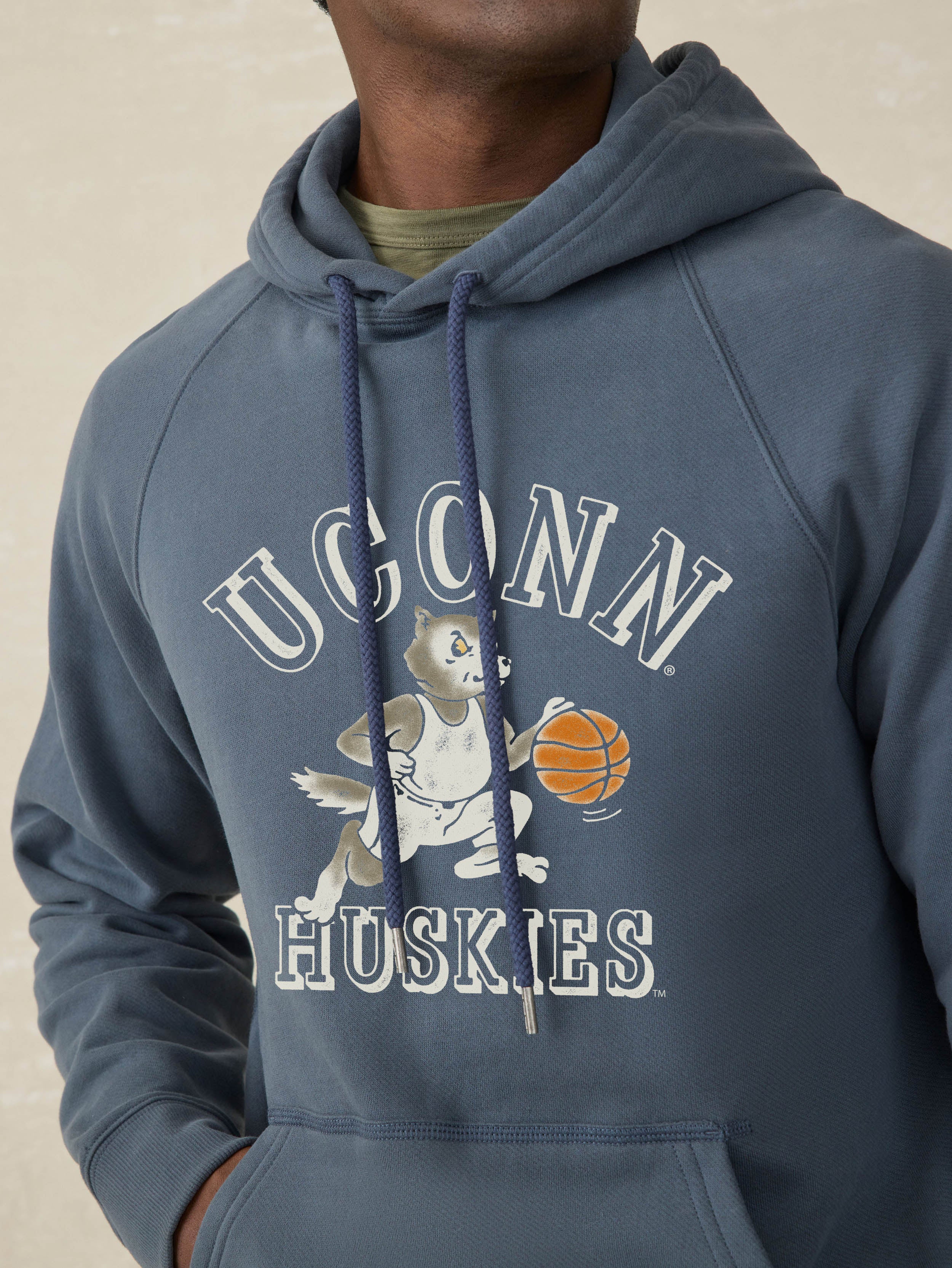 Man wearing a navy blue hoodie with UConn Huskies graphic on the center front against a beige background