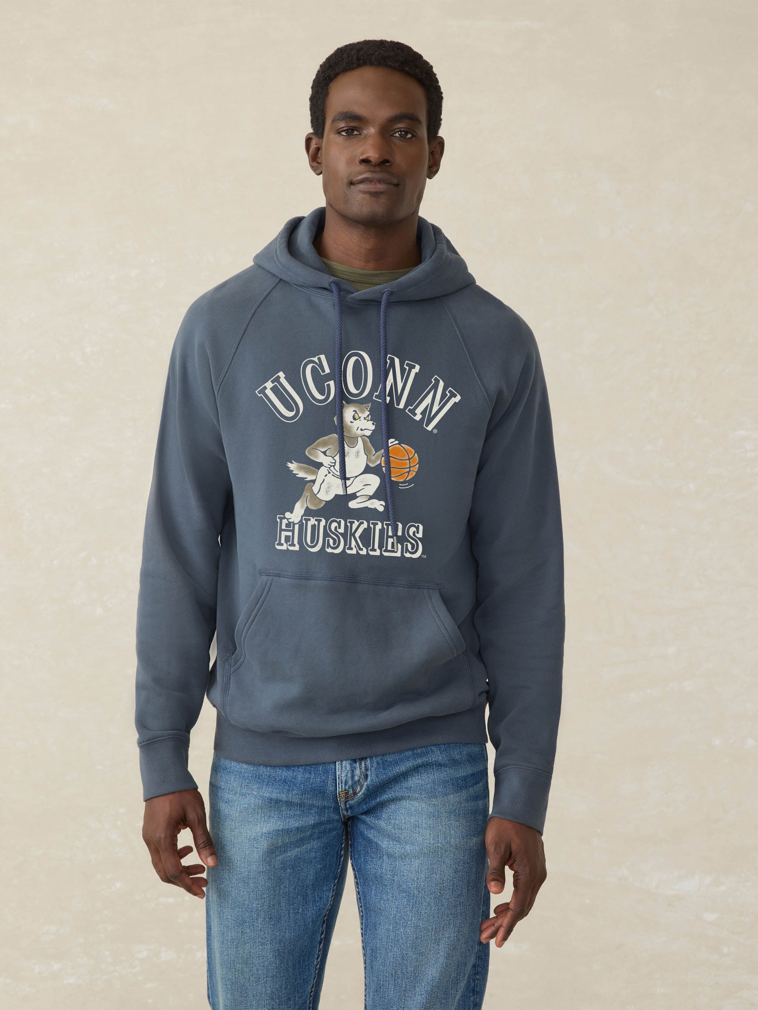Man wearing a navy blue hoodie with UConn Huskies graphic on the center front against a beige background