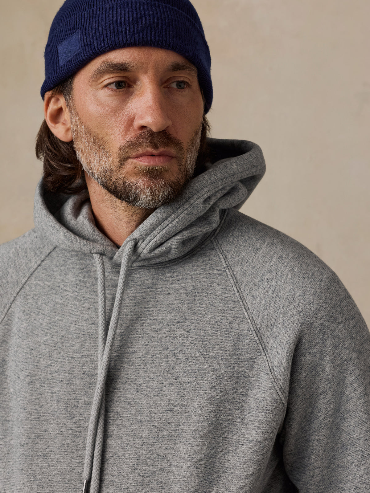 A man wearing a heather gray pullover hoodie and blue beanie, image 3 of 7