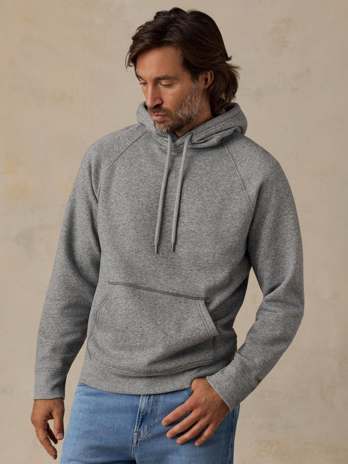 A man wearing a heather gray pullover hoodie paired with blue jeans, image 2 of 7