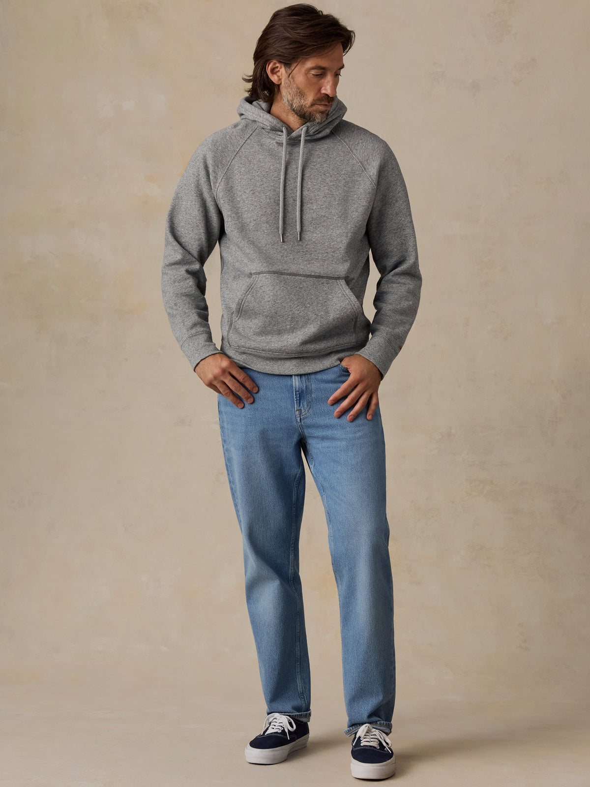A man wearing a heather gray pullover hoodie paired with blue jeans, image 6 of 7
