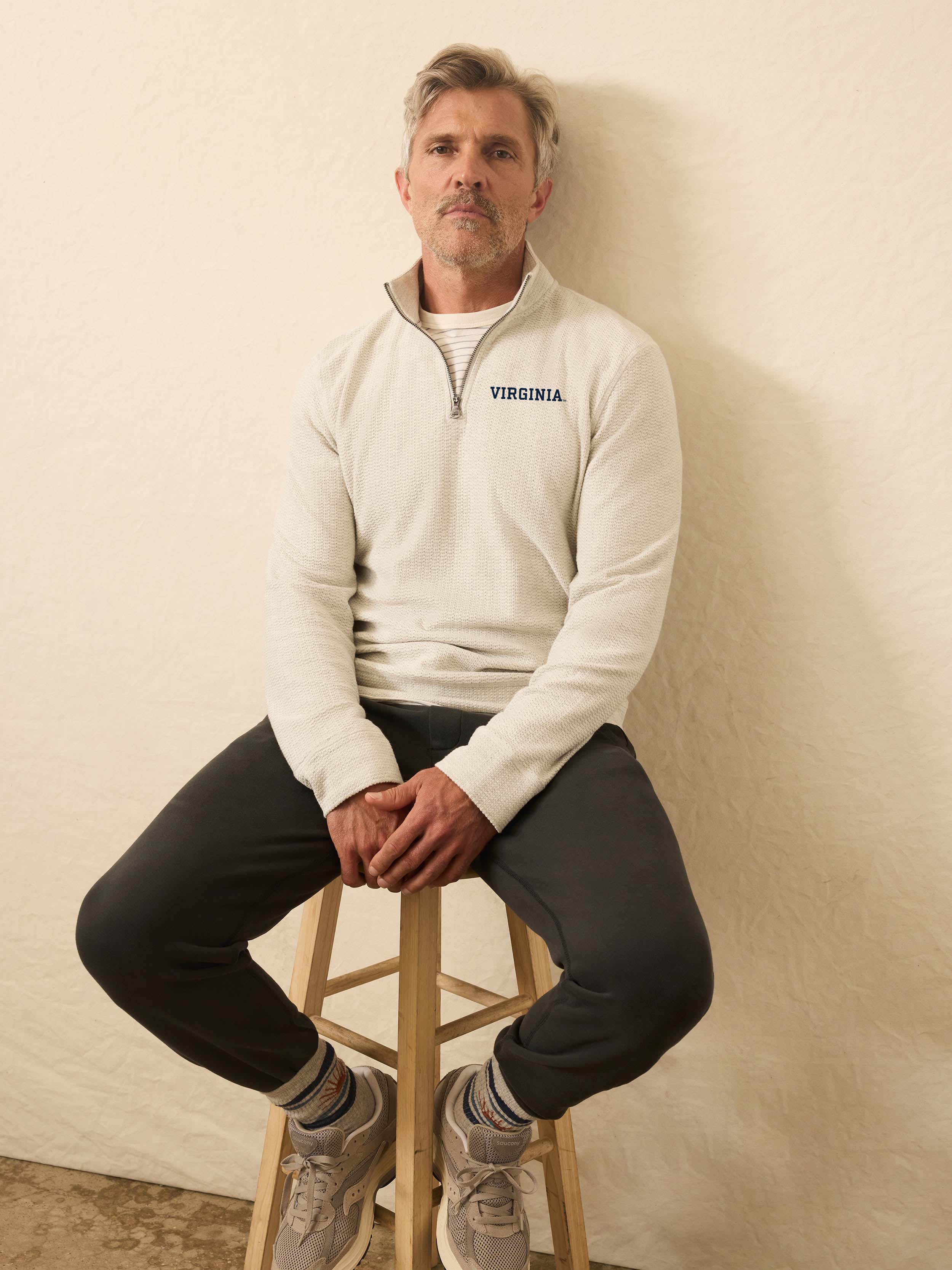 Man is wearing a heather grey quarter zip sweatshirt with University of Virginia logo on the left chest against a beige background