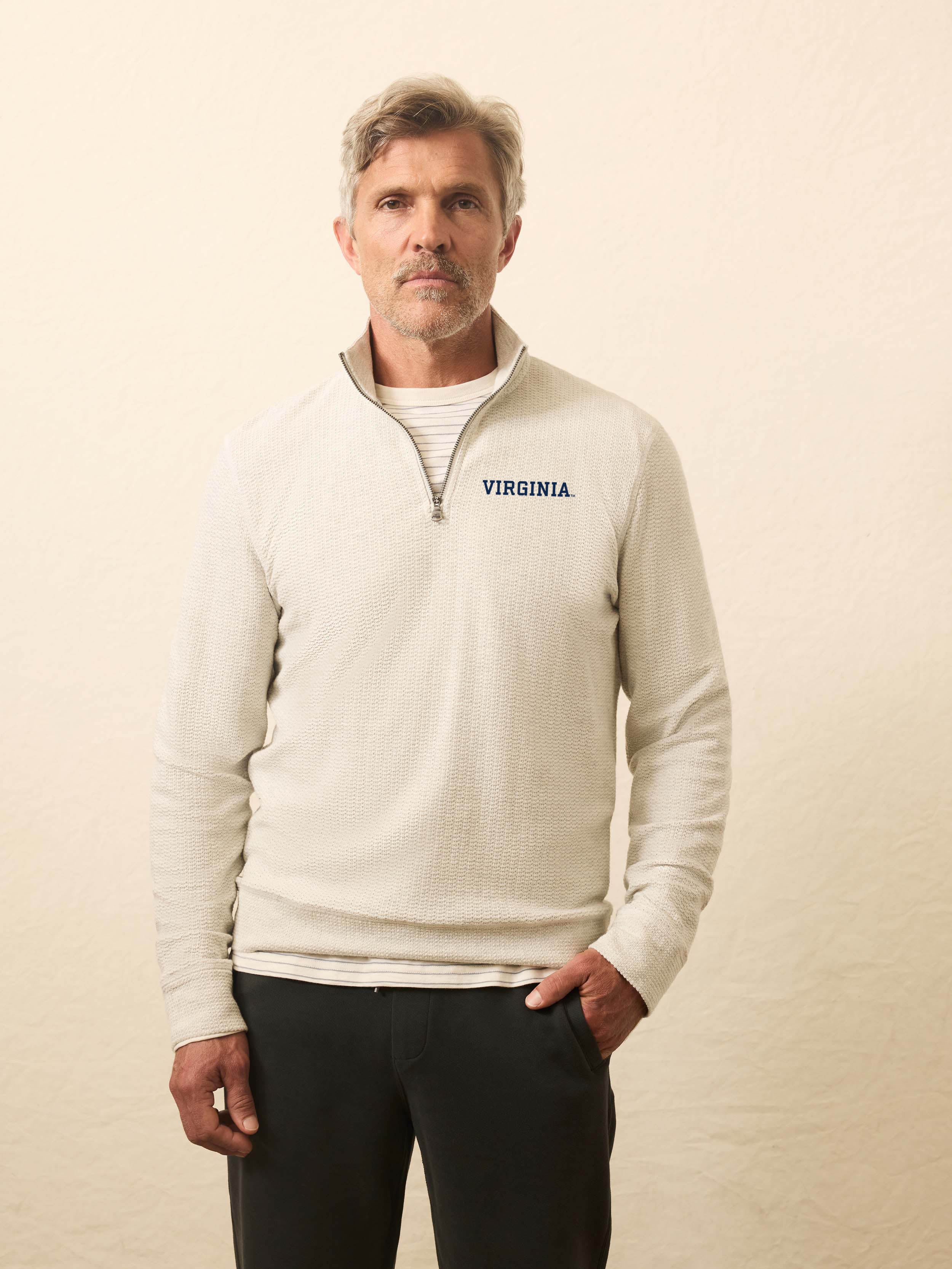 Man is wearing a heather grey quarter zip sweatshirt with University of Virginia logo on the left chest against a beige background