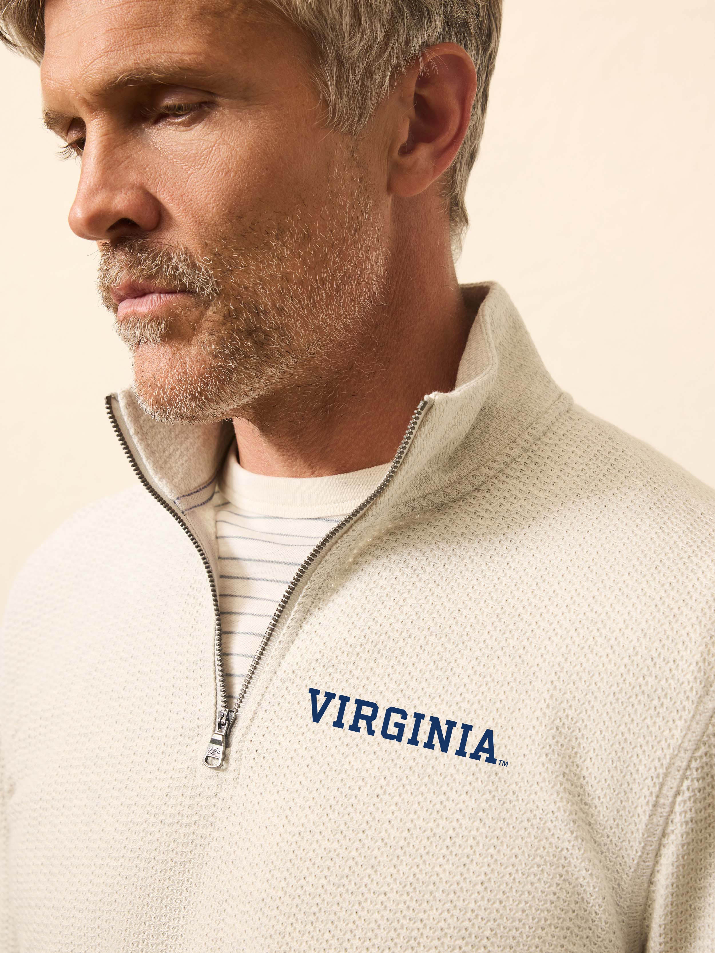 Man is wearing a heather grey quarter zip sweatshirt with University of Virginia logo on the left chest against a beige background