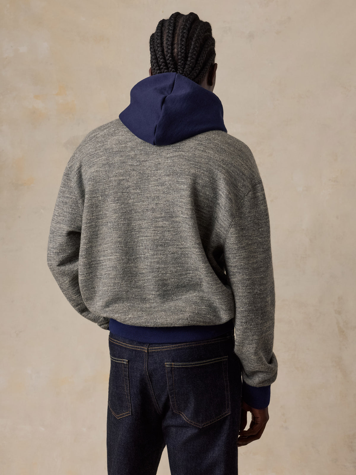 A man viewed from behind wearing a blue and grey hoodie with blue jeans, image 5 of 5