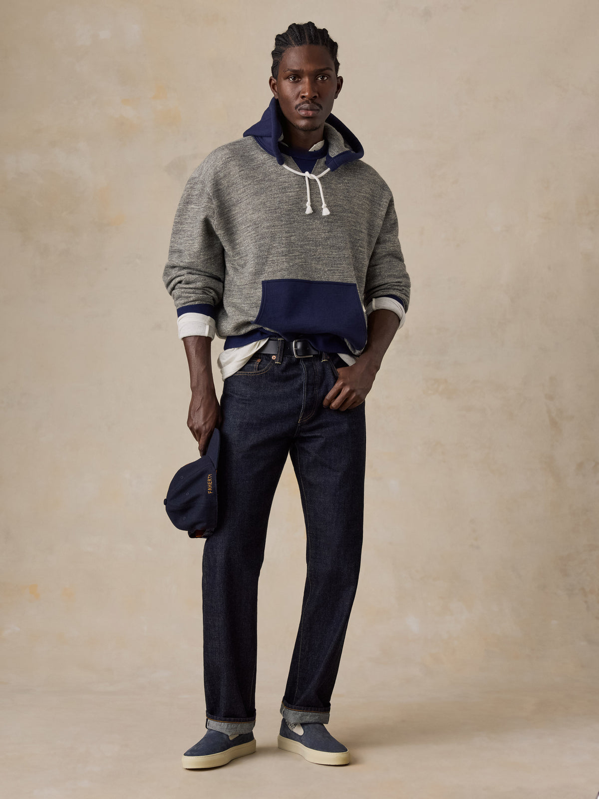 A man wearing a blue and grey hoodie with blue jeans, image 2 of 5