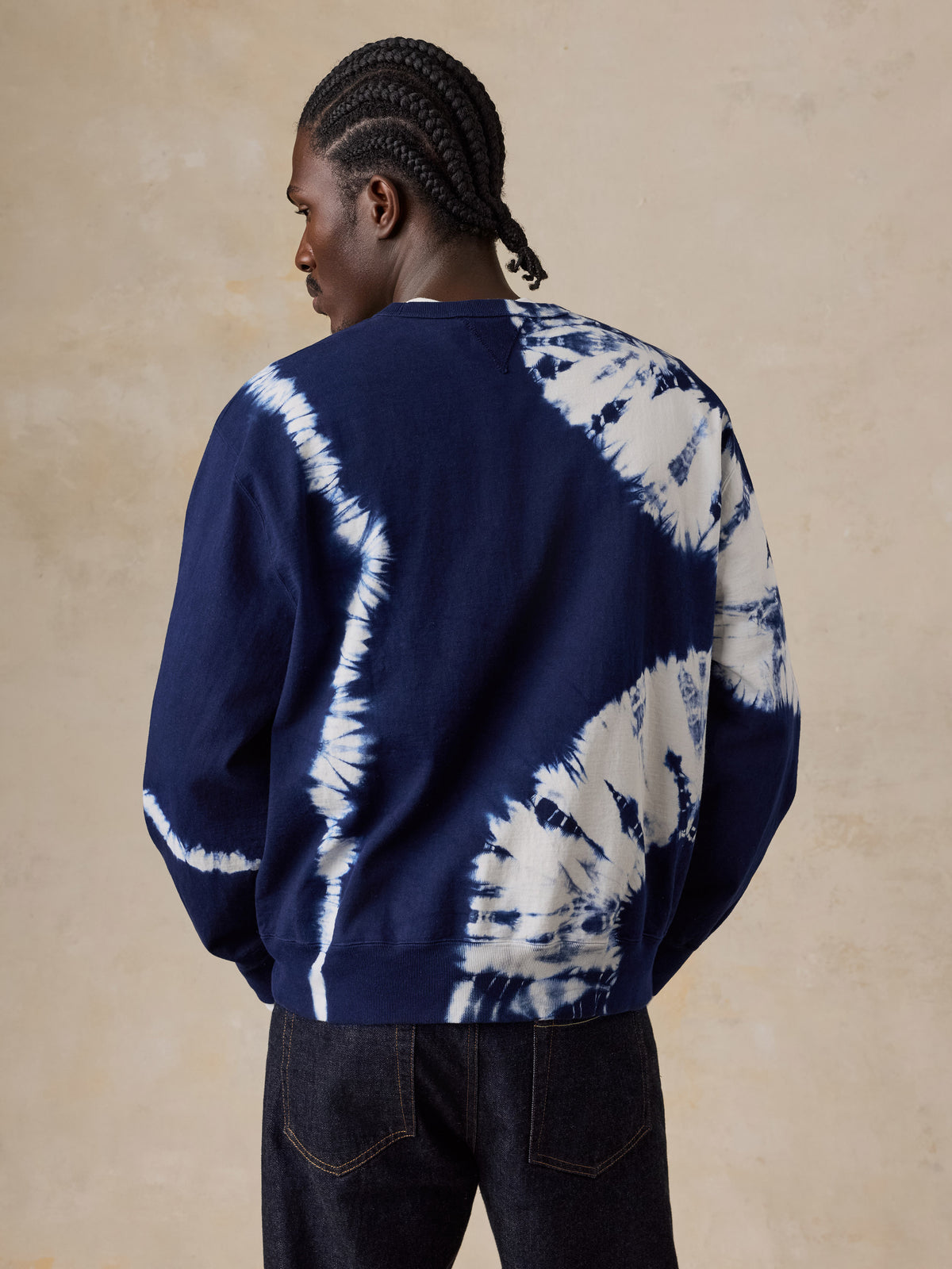 A man viewed from behind wearing a shibori dyed sweatshirt and blue jeans, image 4 of 6